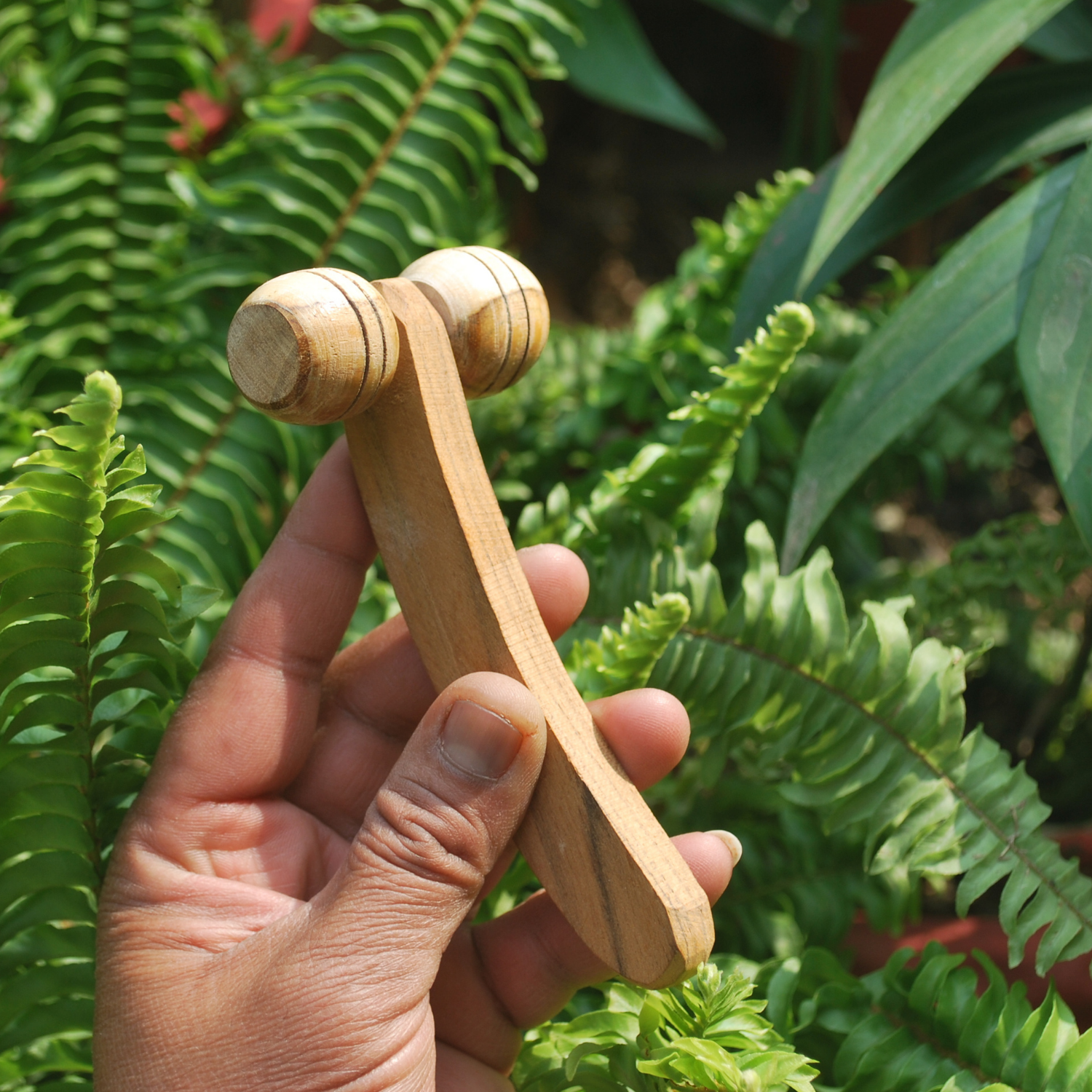 lifestyle image of the Side view of a handmade wooden lymphatic face roller showing the curved handle, dual rollers and natural wood grain.