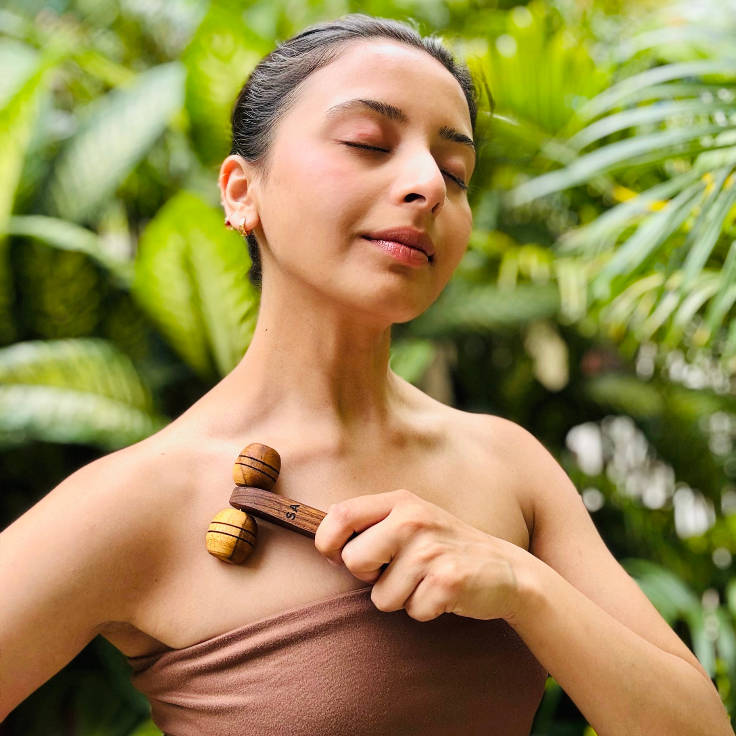 Woman using a wooden lymphatic face roller around the collarbone and upper chest during a wellness routine.