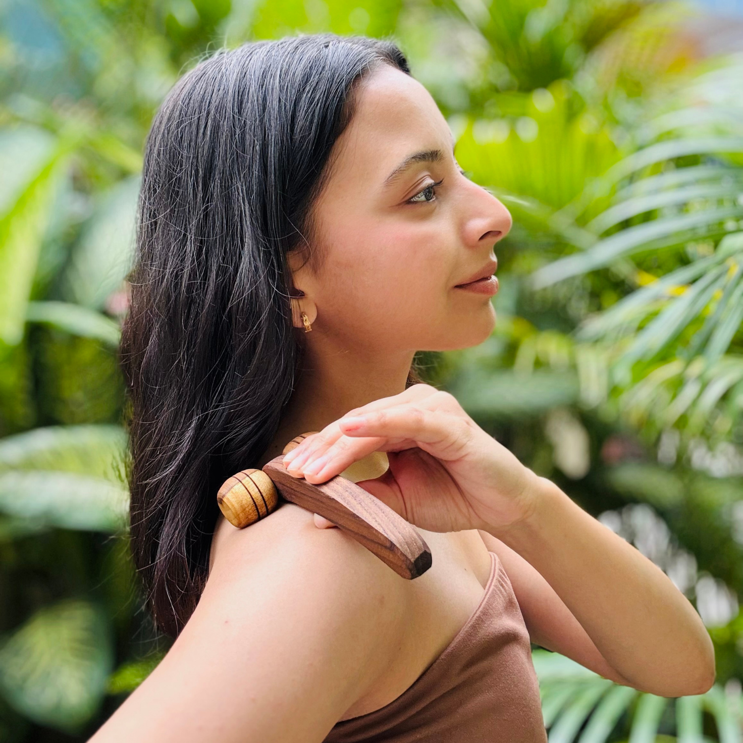 Woman using a wooden lymphatic face roller across the shoulder as part of a relaxing body-care routine.
