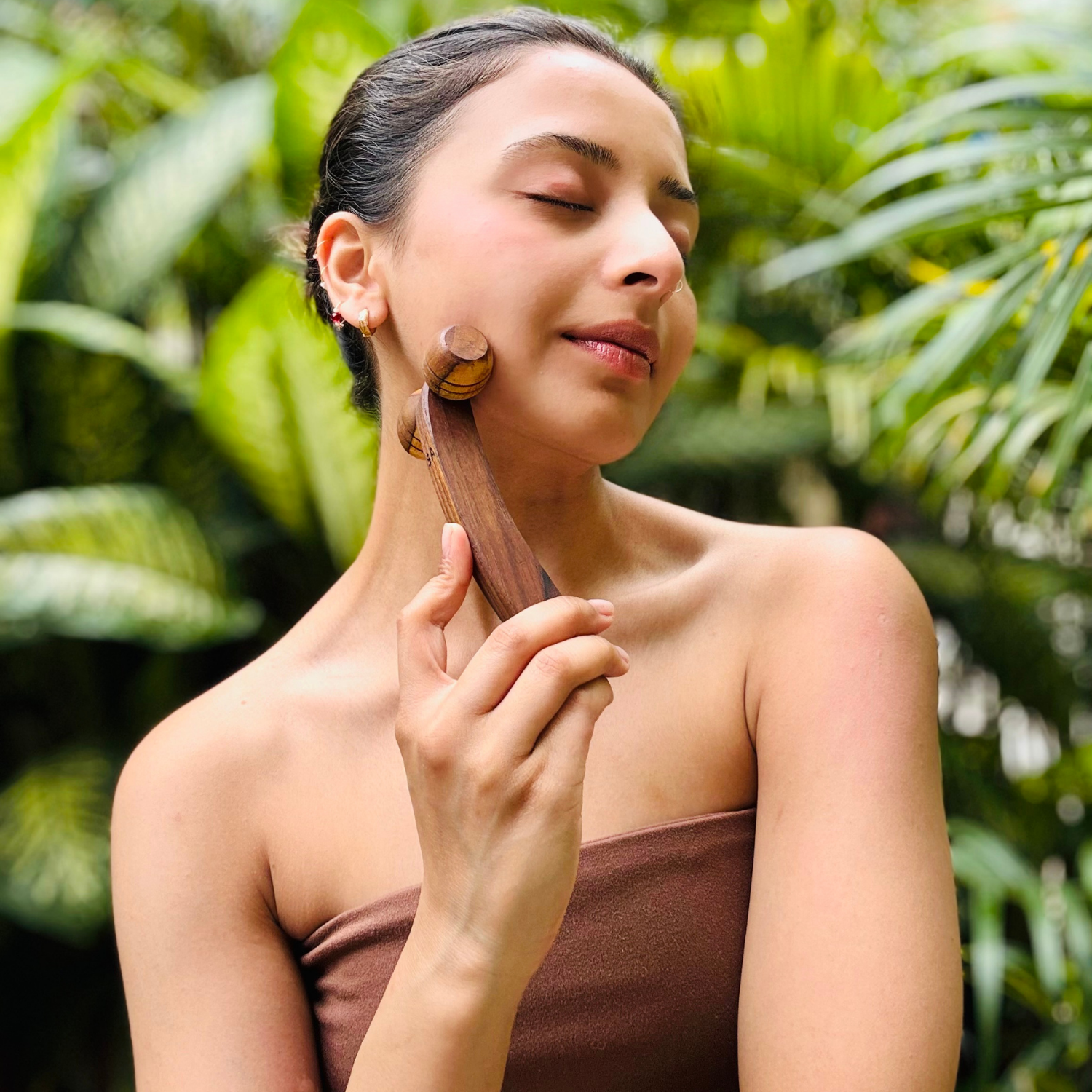 Woman gently using a wooden lymphatic face roller along the jawline and side of the face.