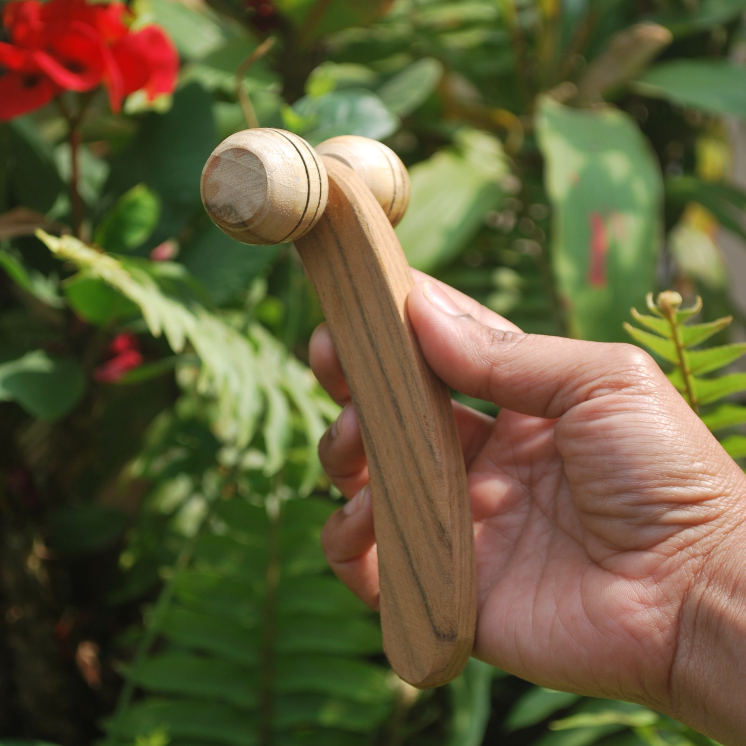 Handmade wooden lymphatic face roller with dual rounded rollers and a curved wooden handle, held outdoors in hand.