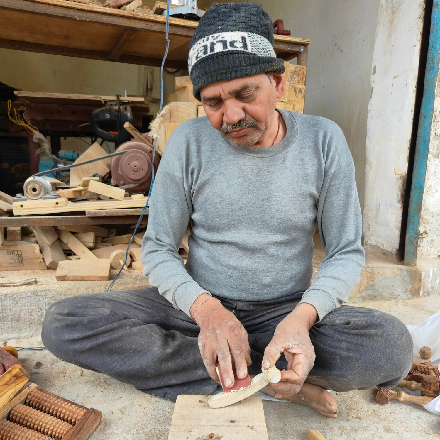 Indian artisan hand-finishing a wooden lymphatic face roller in a traditional woodworking workshop.