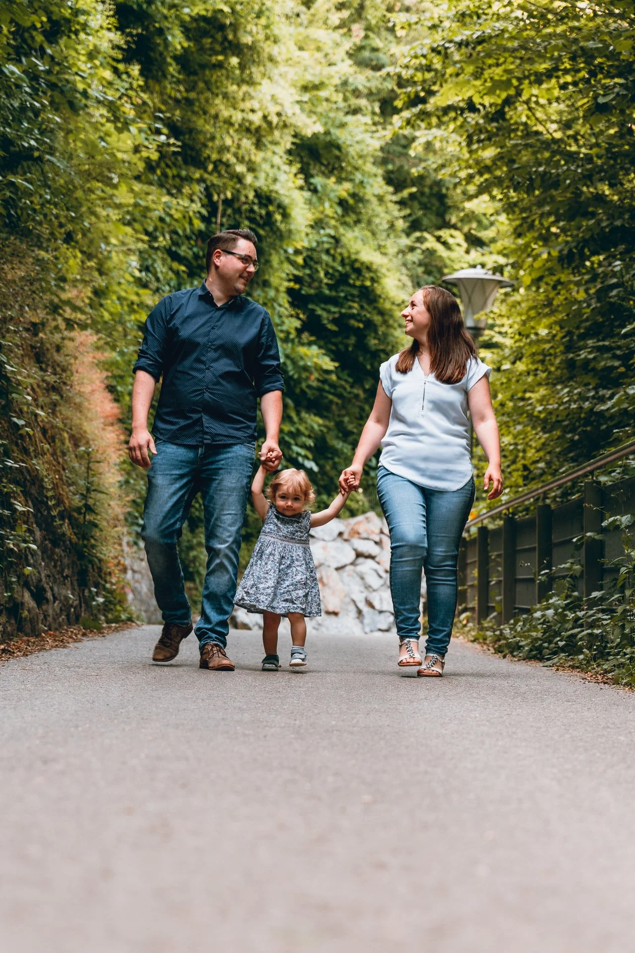 Family walking on a forest path holding hands, surrounded by lush greenery.