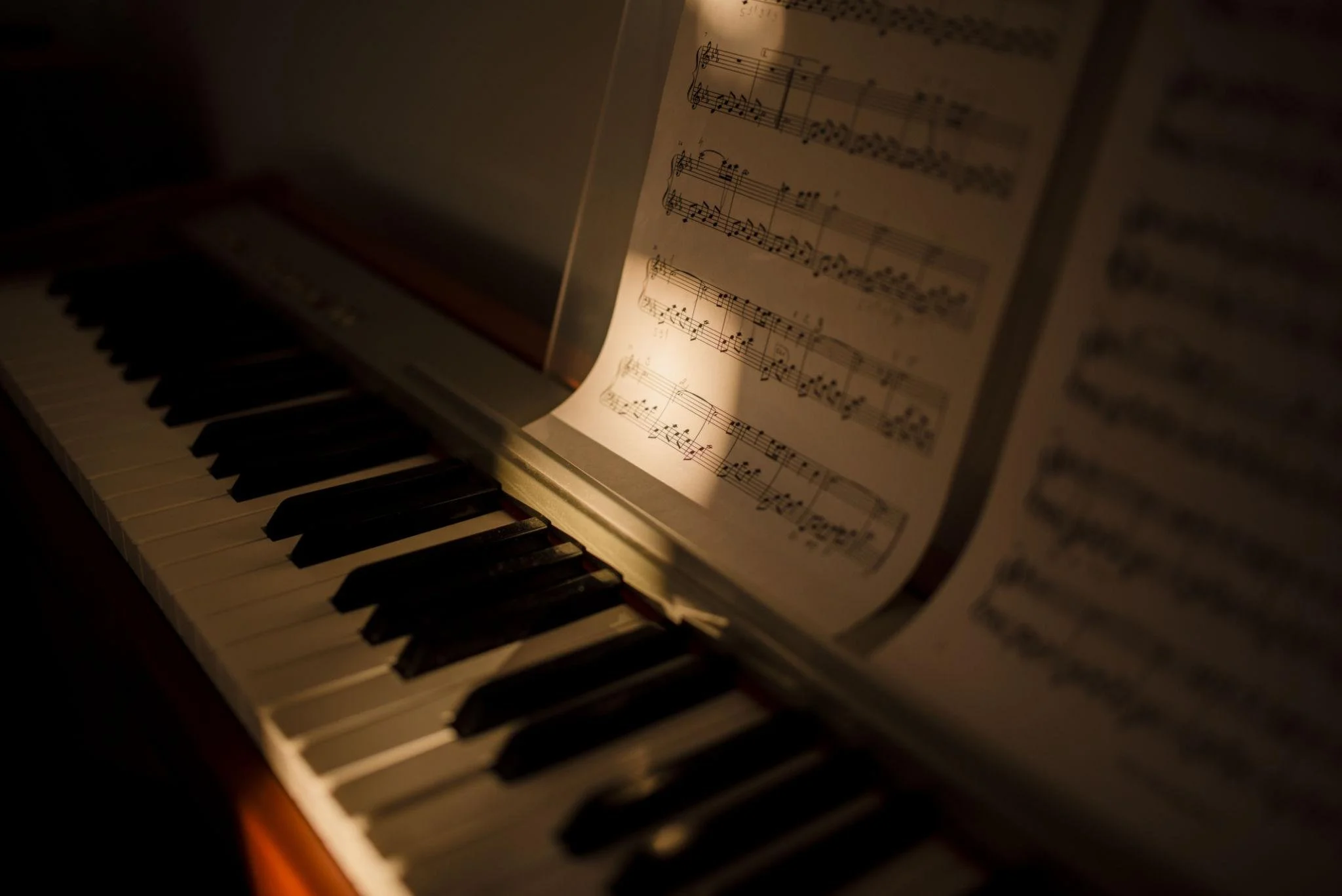 Close-up of a piano keyboard with sheet music illuminated by a warm light.