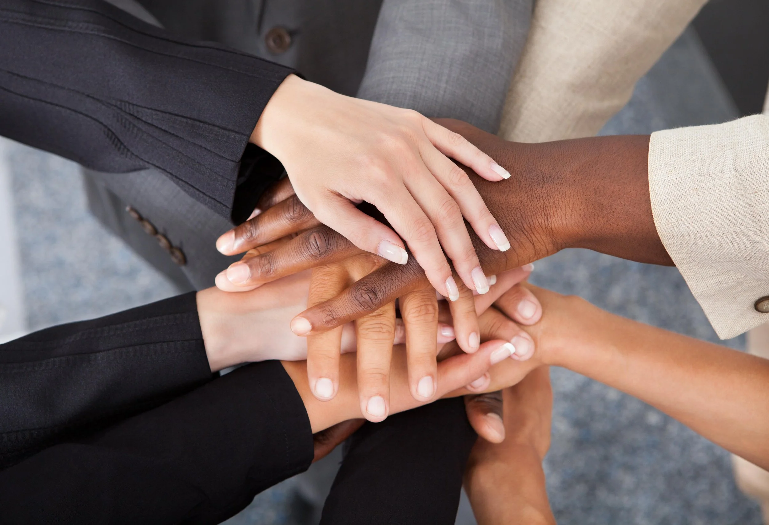 Multiple hands from diverse individuals stacking together in a show of unity and teamwork