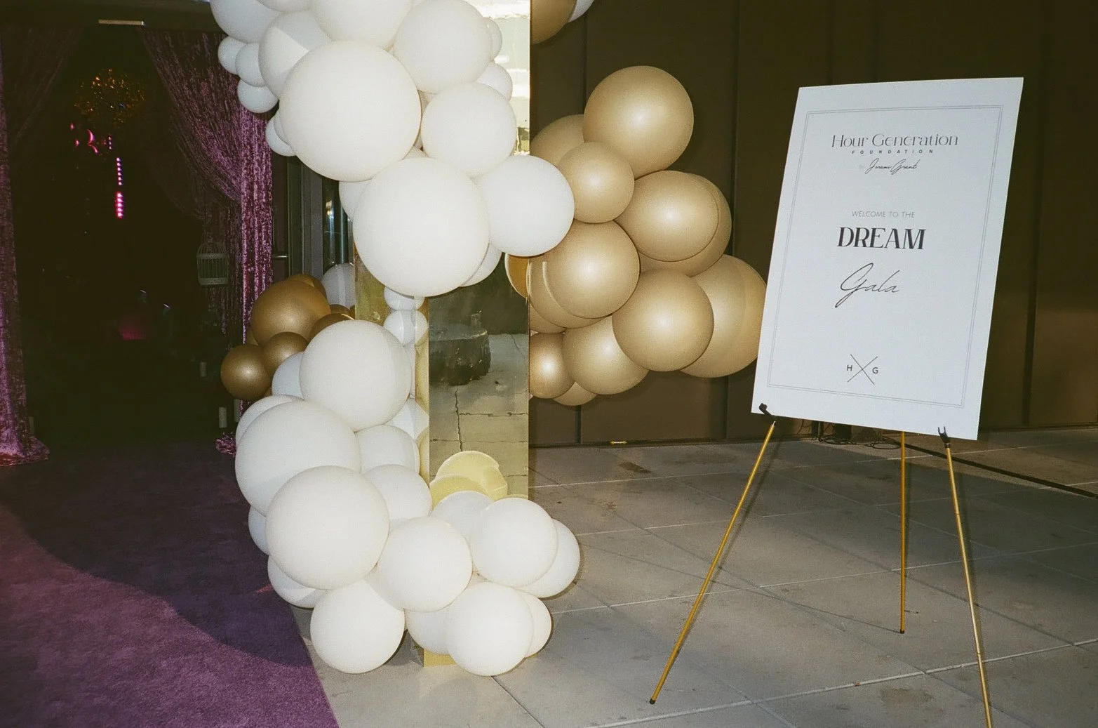 White and gold balloons arranged near a sign that reads 'Hour Generation Foundation Welcome to the Dream Gala' with the initials H G.