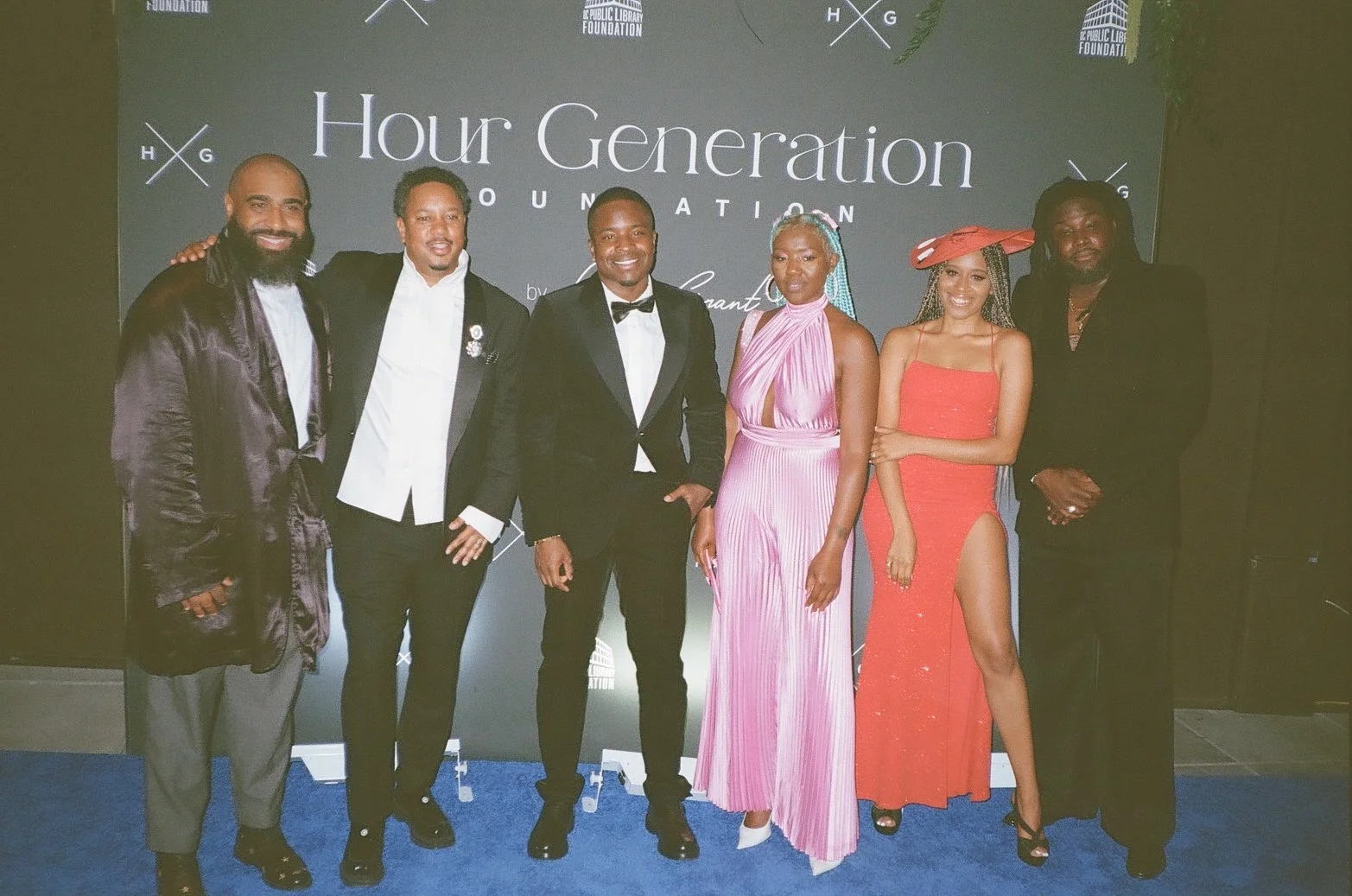 Group of six people dressed in formal attire standing in front of a backdrop with text that reads 'Hour Generation Foundation' and logos. They are smiling and posing for the photo.