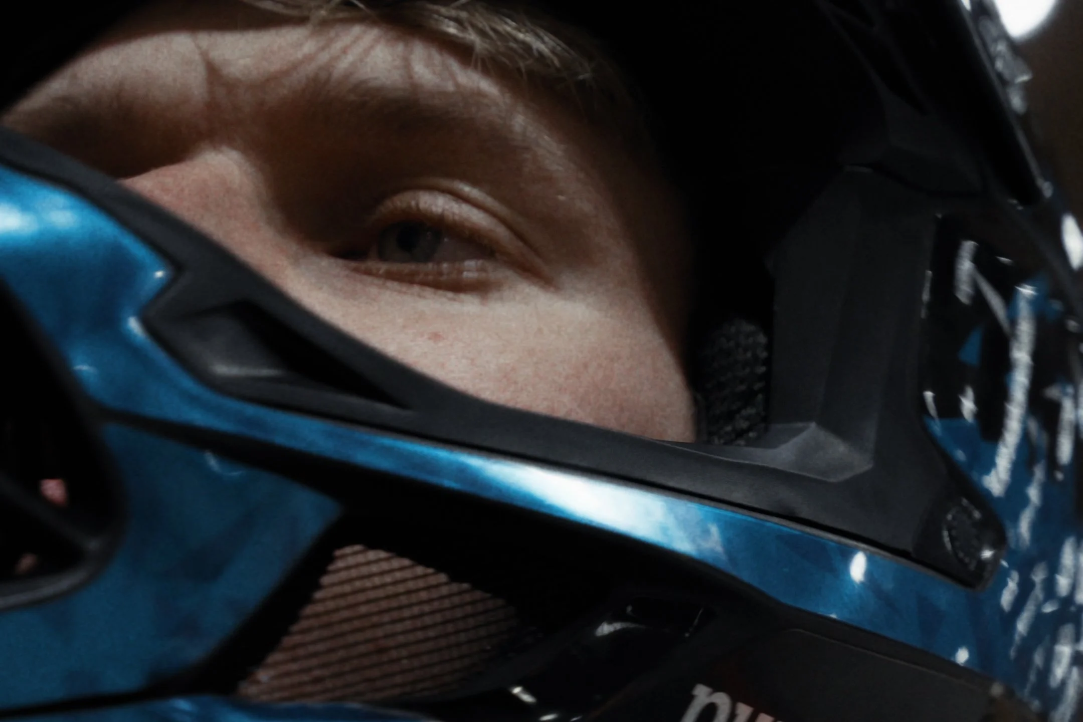 Close-up of a person's face partially visible through a blue and black bycicle helmet, looking to the left.