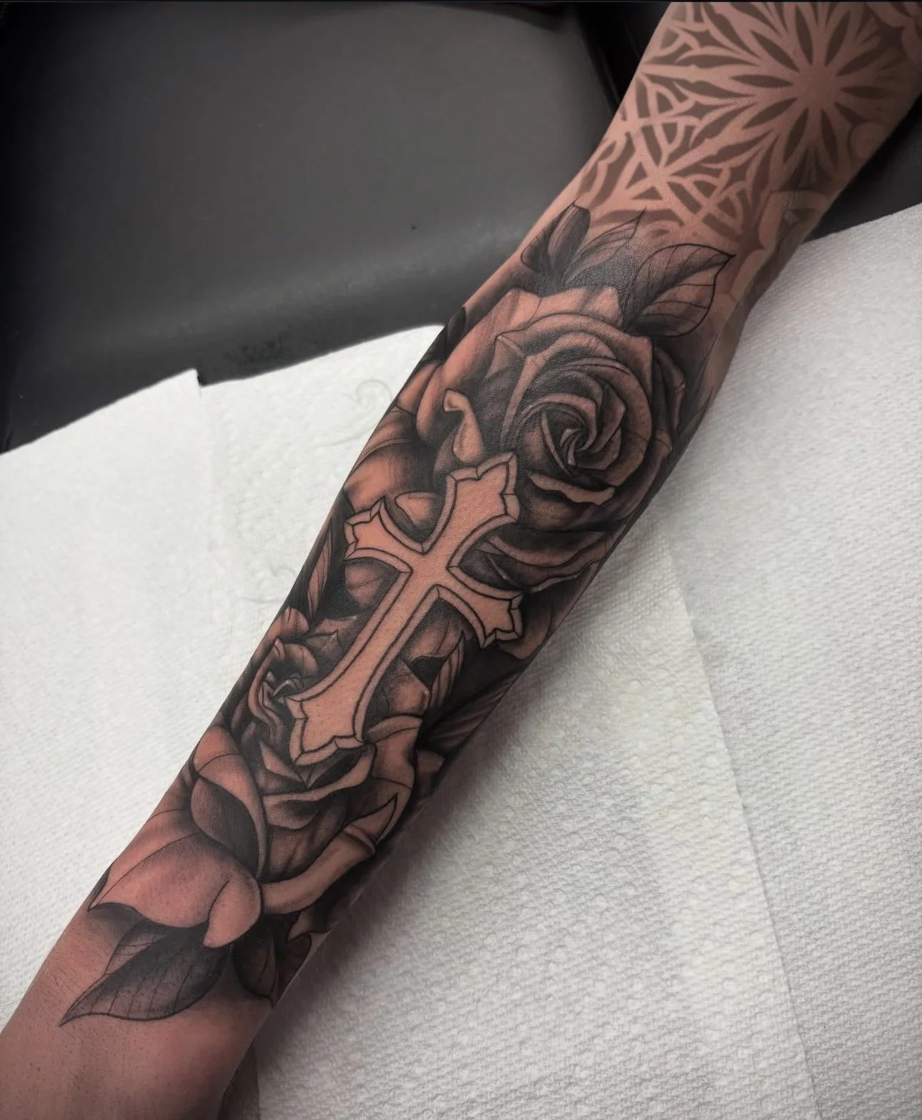 black and grey cross with roses behind it on a forearm, portfolio work by Brooke Canzoneri at sink or swim tattoo and piercing in Niagara Falls, ny