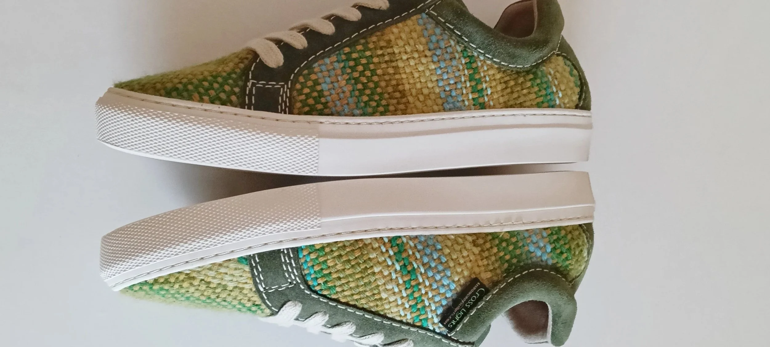 Pair of casual sneakers with a woven fabric upper in shades of green, yellow, and blue, white rubber soles, and black accents with white stitching, photographed upside down.