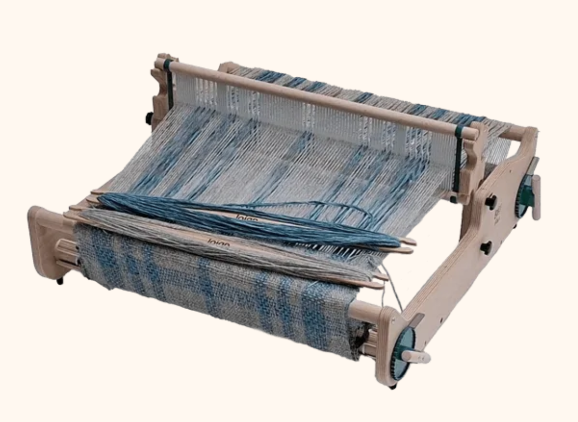 A weaving loom with partially woven textile fabric in shades of blue and gray.