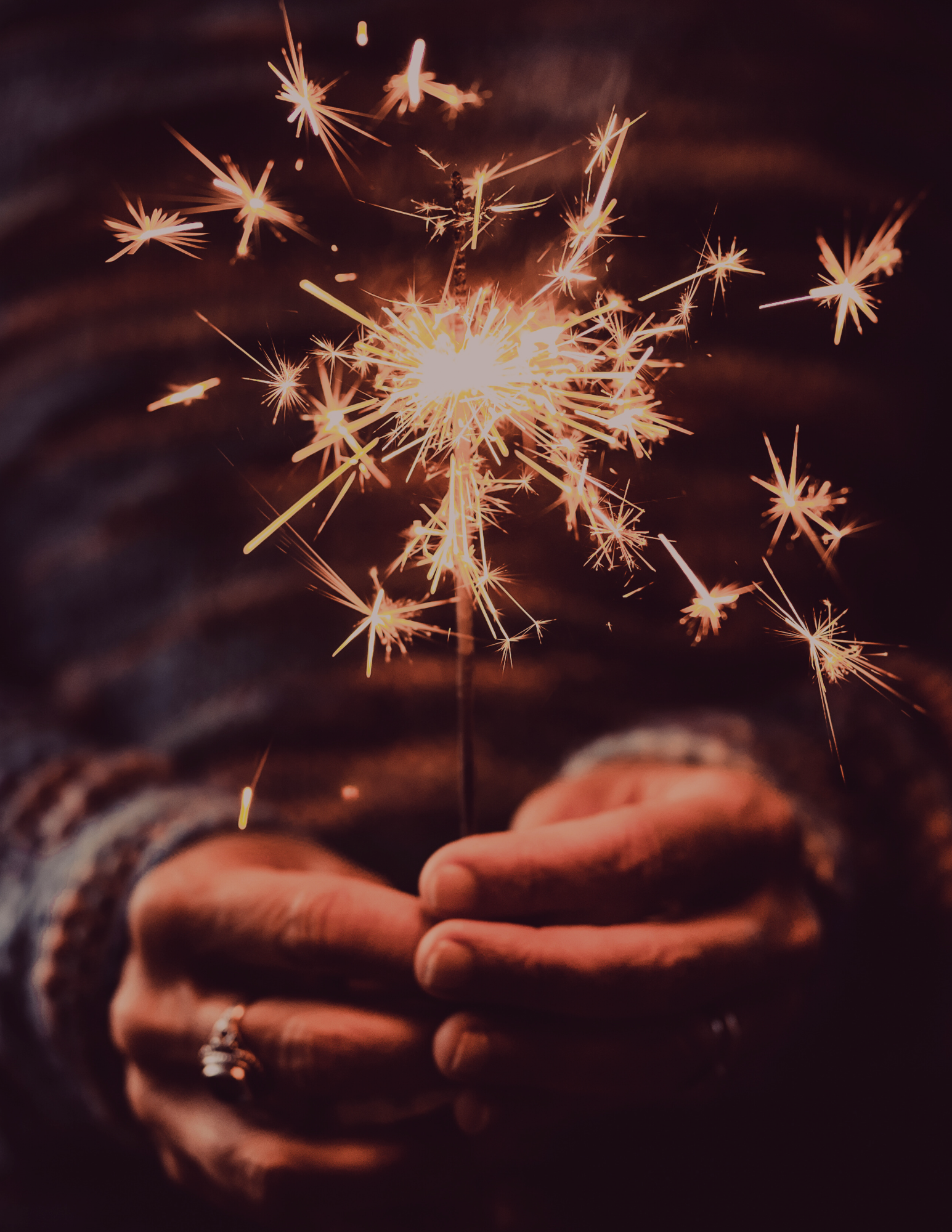 Person holding a lit sparkler with sparks flying in the dark.