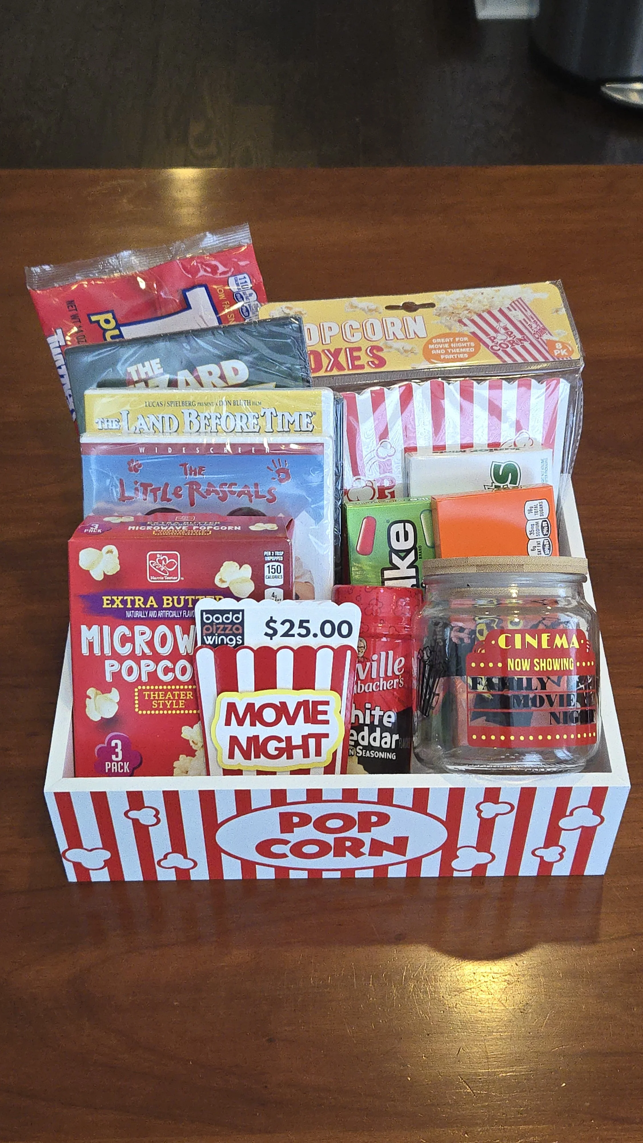 Movie night gift basket in a striped popcorn box, filled with microwave popcorn, boxed candy, and snacks