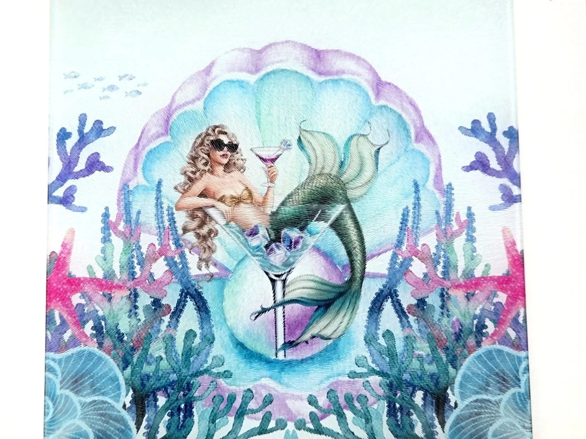 Square glass cutting board printed with a mermaid in sunglasses lounging in a martini glass among coral and seaweed
