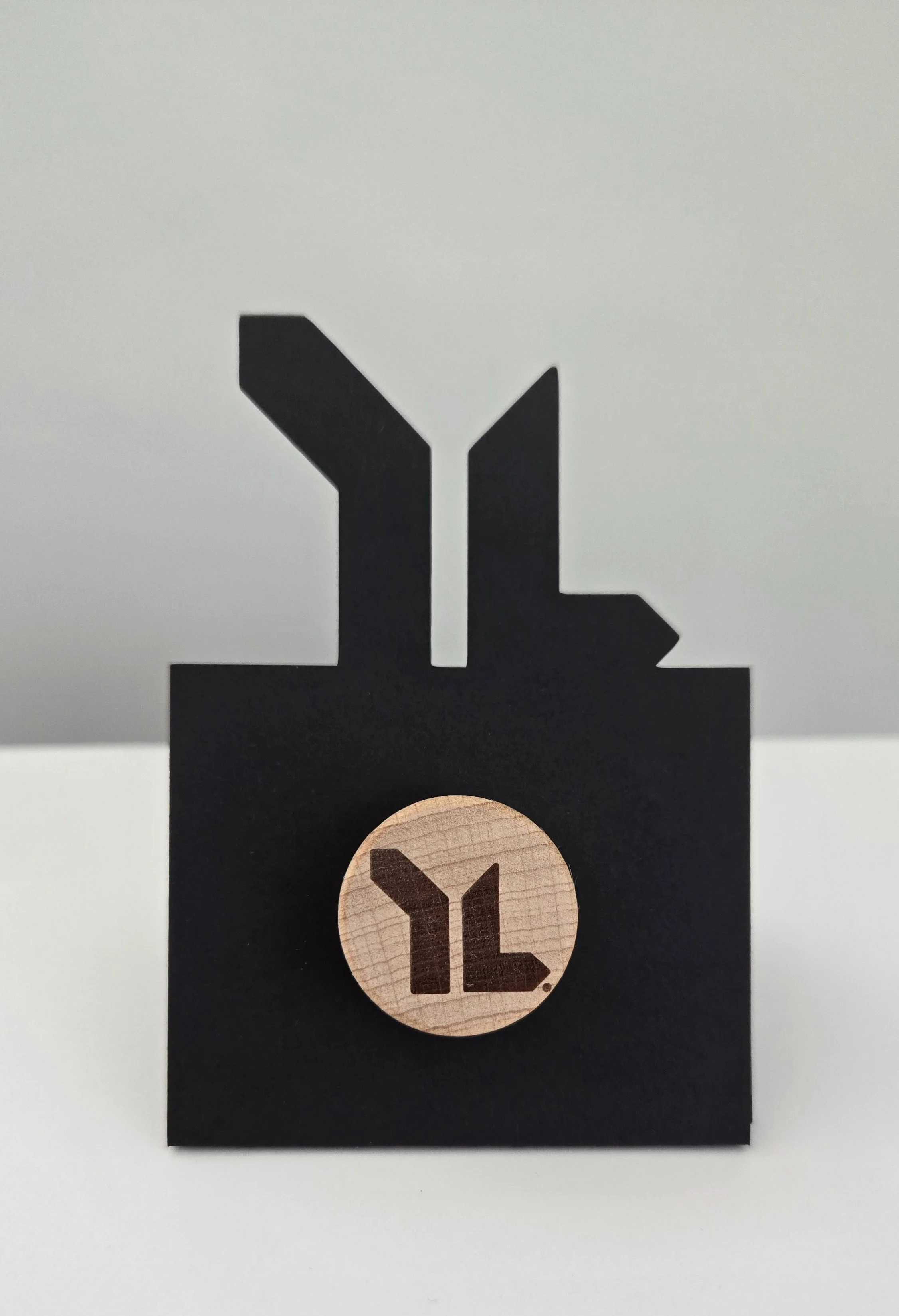Black bottle stopper holder cut in the shape of the Young Life logo, holding a round wooden stopper engraved with the same logo