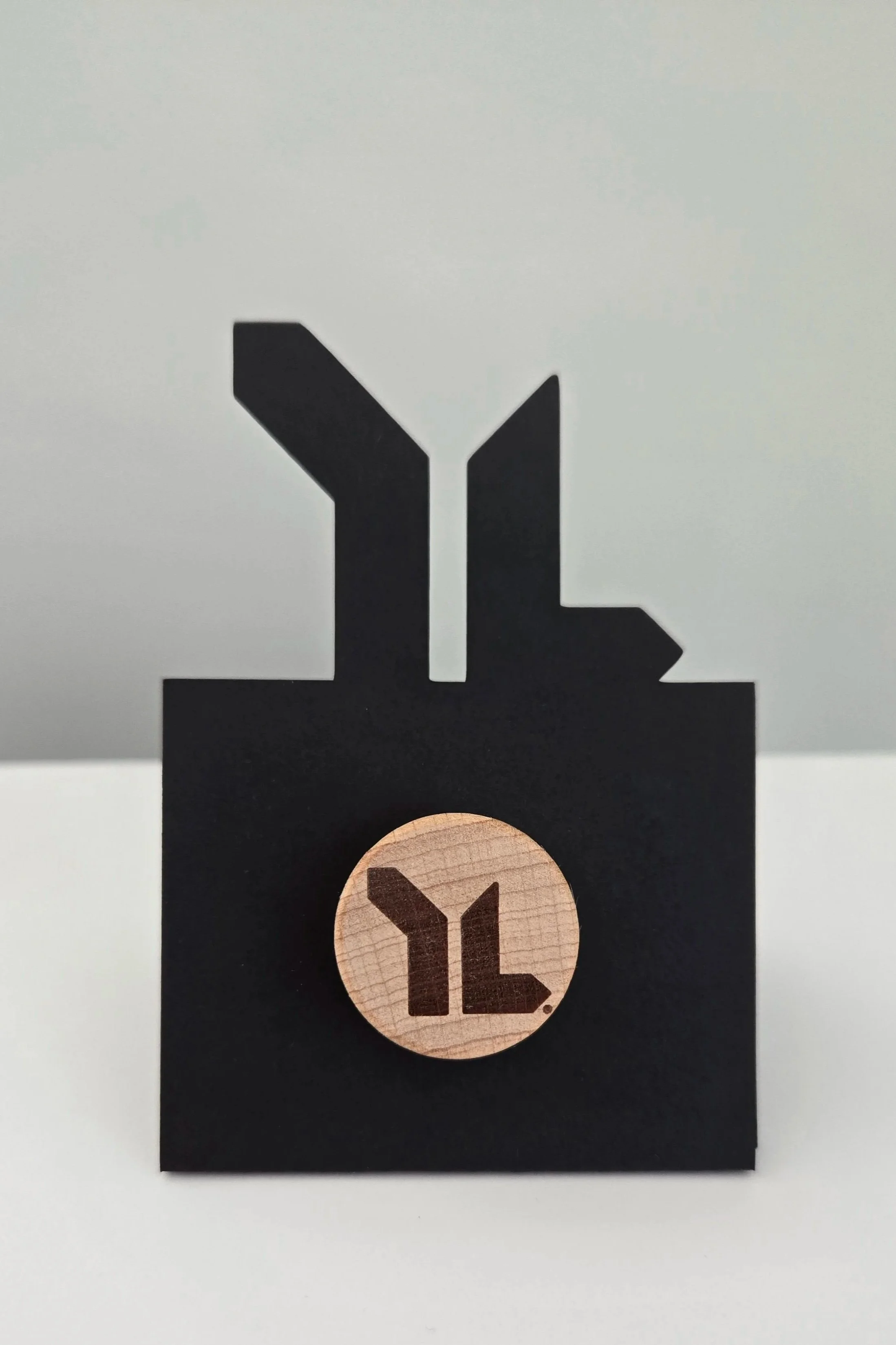 Black paper with a cutout of the Yeti logo, placed on a black card and a wooden circle with the same logo.