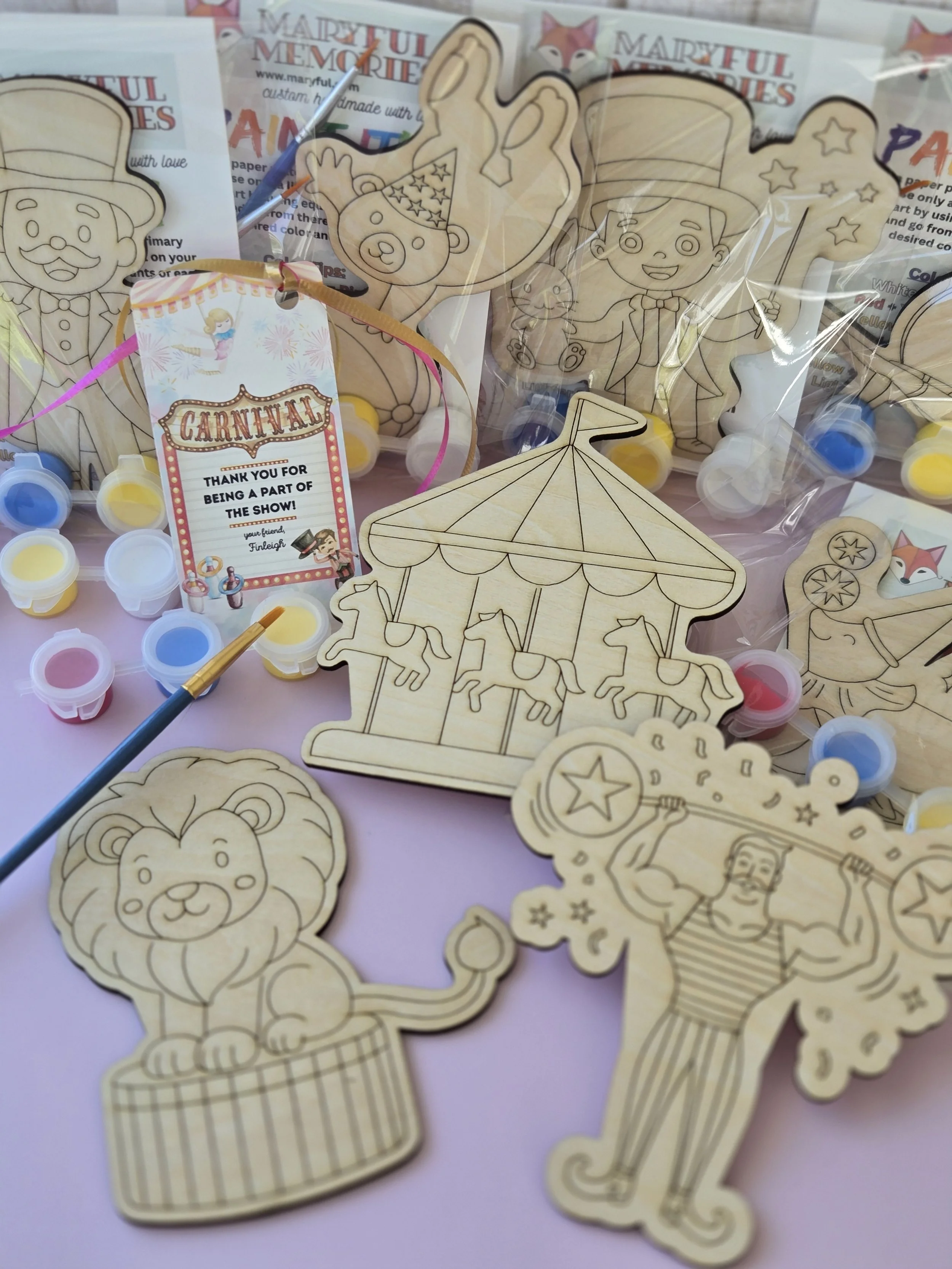 Carnival paint kit with wooden cutouts of a lion, carousel, strongman, and ringmaster, plus paint pots, brushes, and thank-you tags