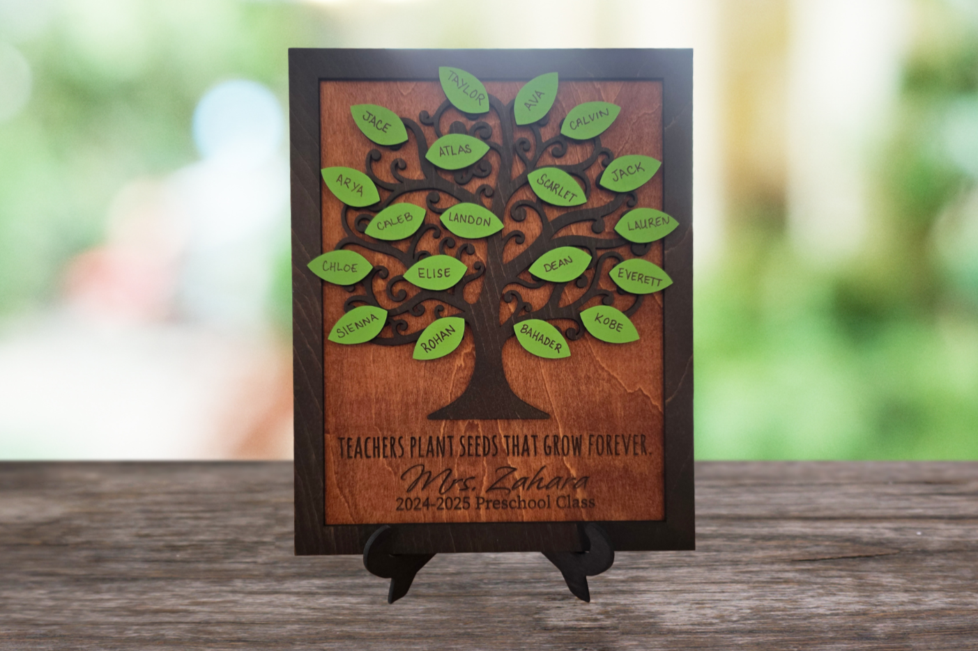 Wooden teacher tree plaque with student names on green leaves and the message Teachers Plant Seeds That Grow Forever