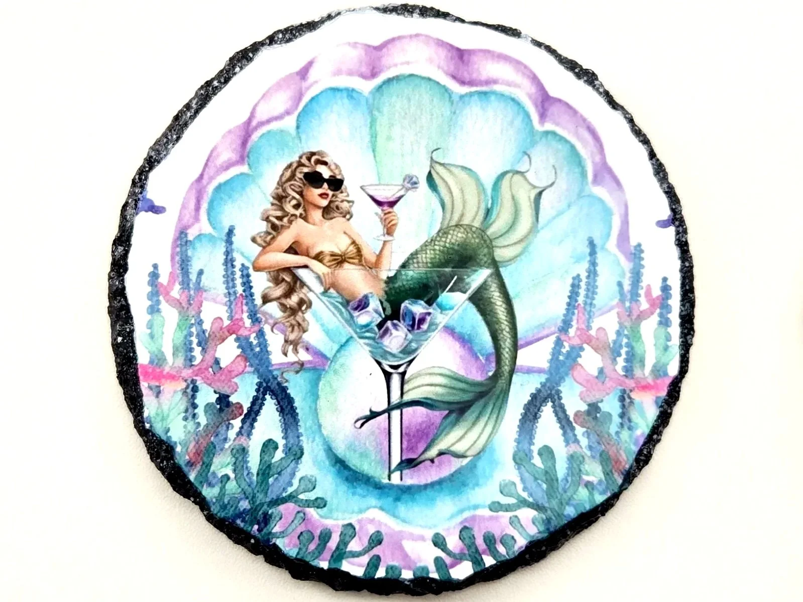 Round slate coaster printed with a mermaid in sunglasses lounging in a martini glass, framed by a seashell and coral