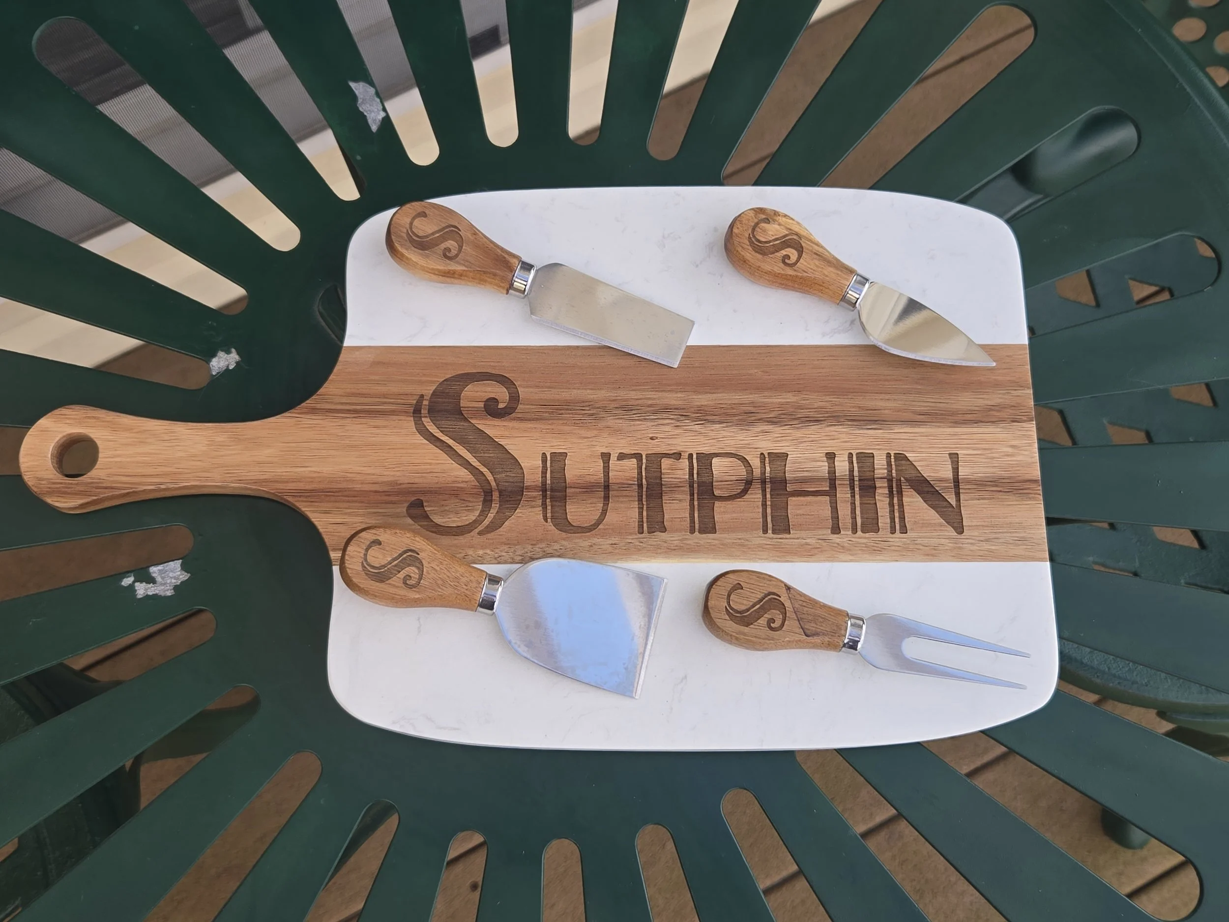 Acacia and white marble charcuterie board engraved with a family name, with four cheese knives engraved with a matching initial