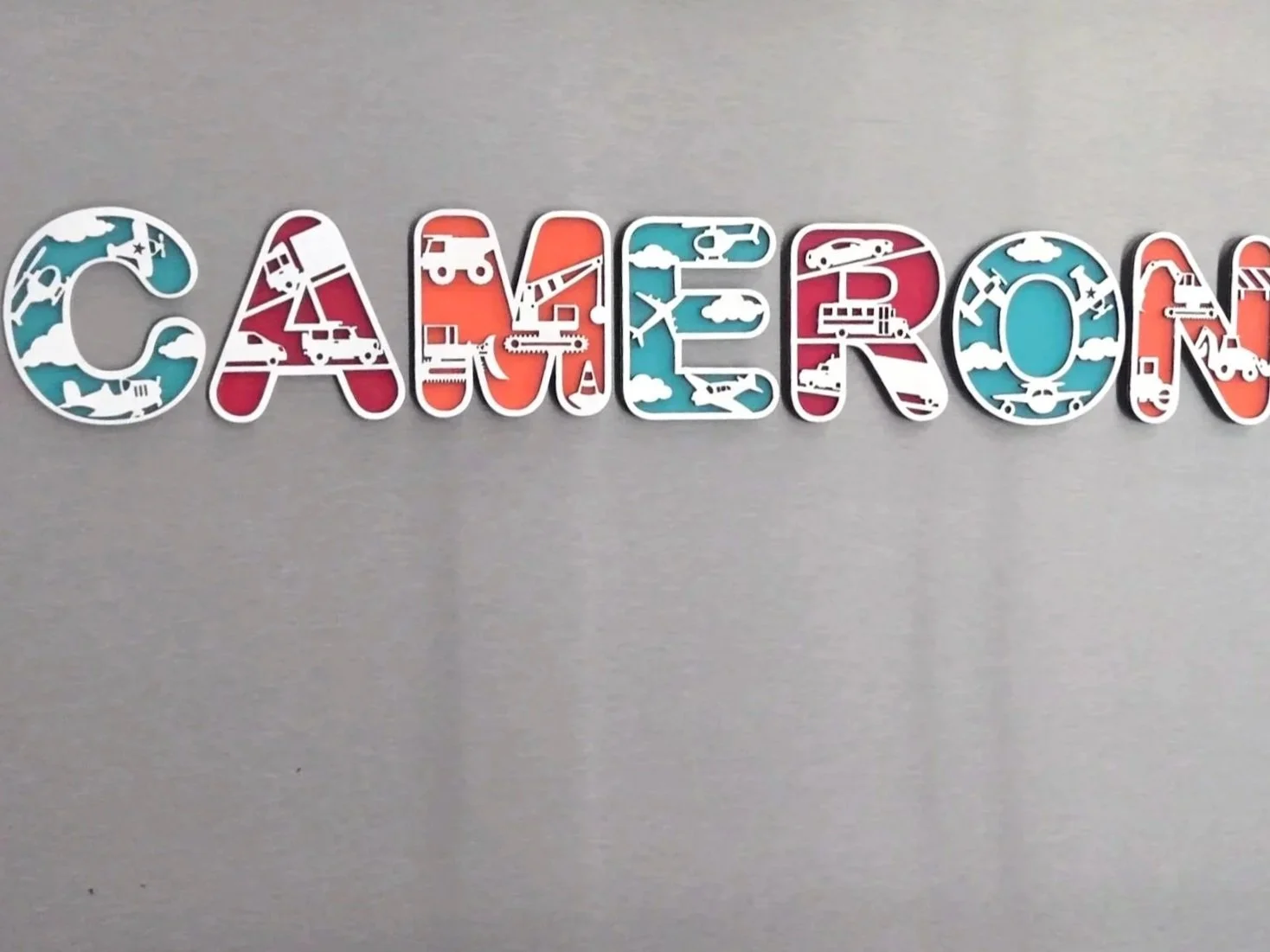 Letter magnets spelling a child's name, each letter filled with cars, trucks, and airplanes in teal, red, and white