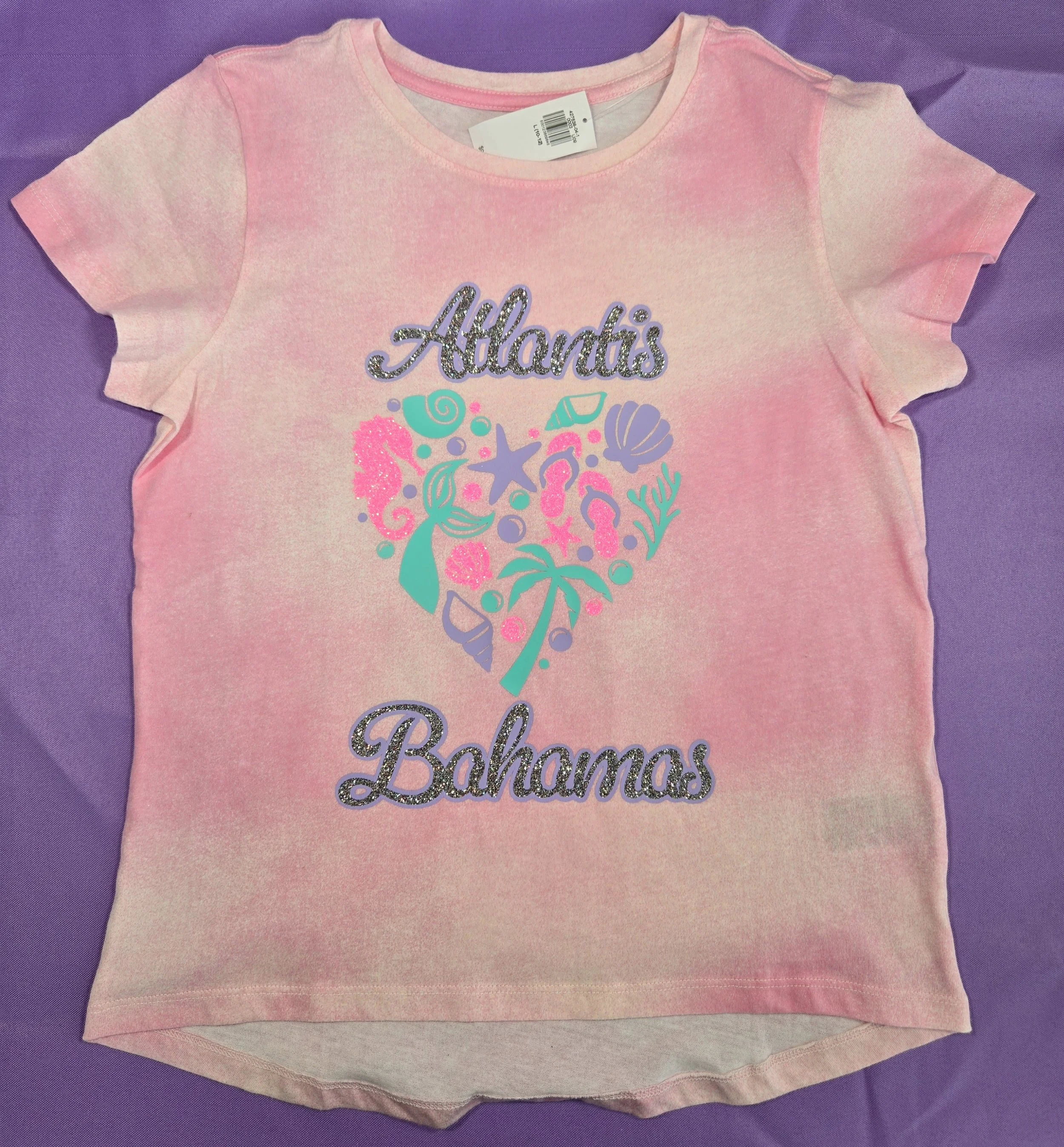 Pink tie-dye kids' shirt reading Atlantis Bahamas around a heart filled with mermaids, seashells, flip flops, and palm trees