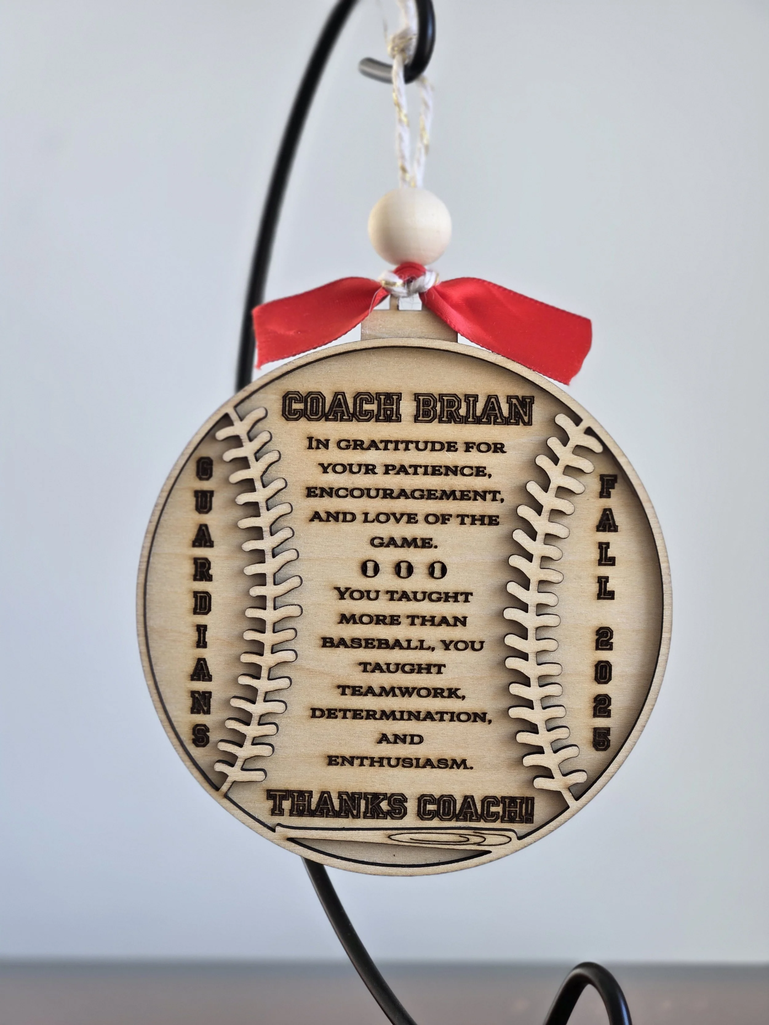 Round baseball-style wooden coach ornament with a thank-you message, team name, and season, tied with a red bow