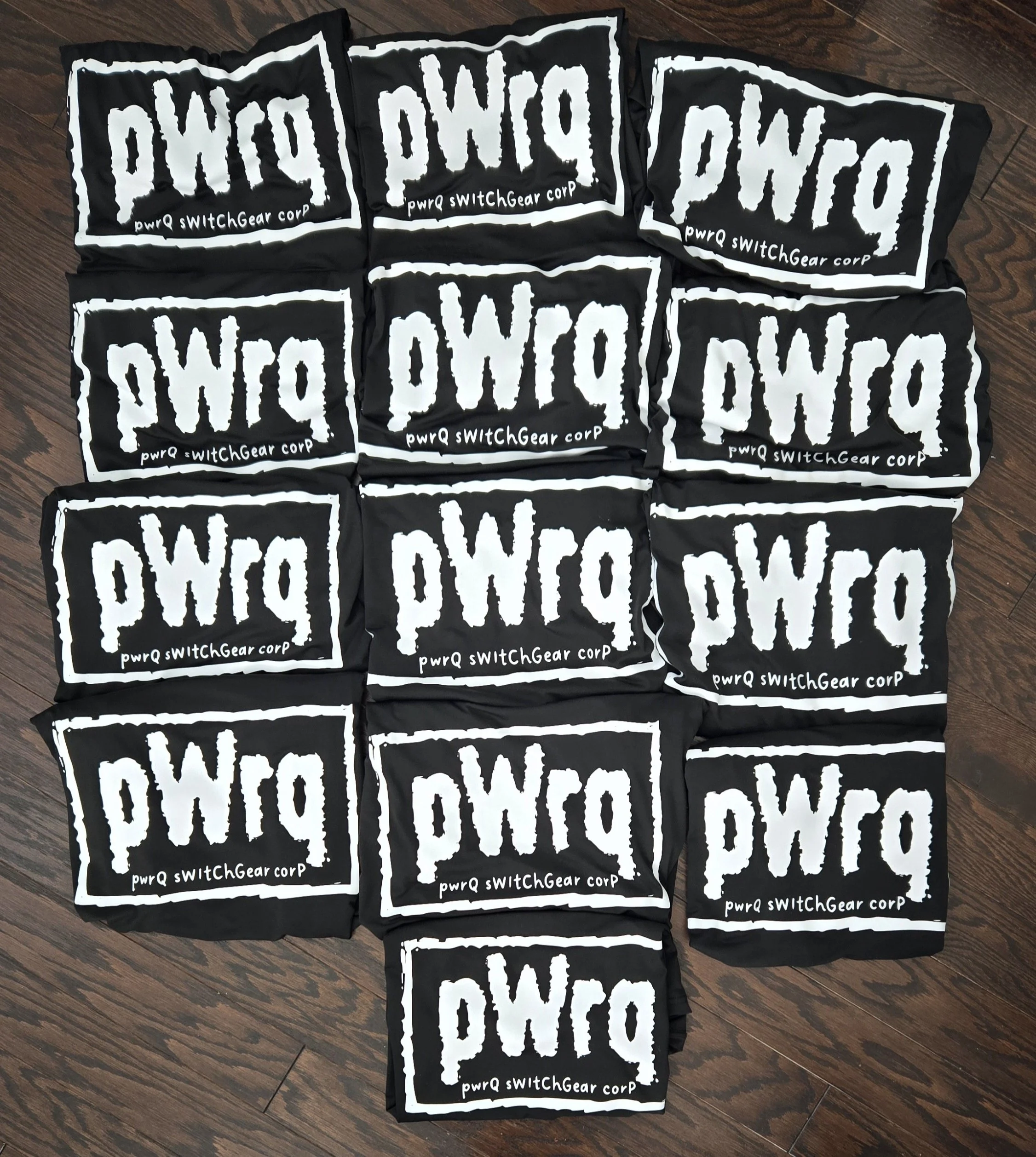 Black company shirts printed with a large white pWrq logo, laid out in rows