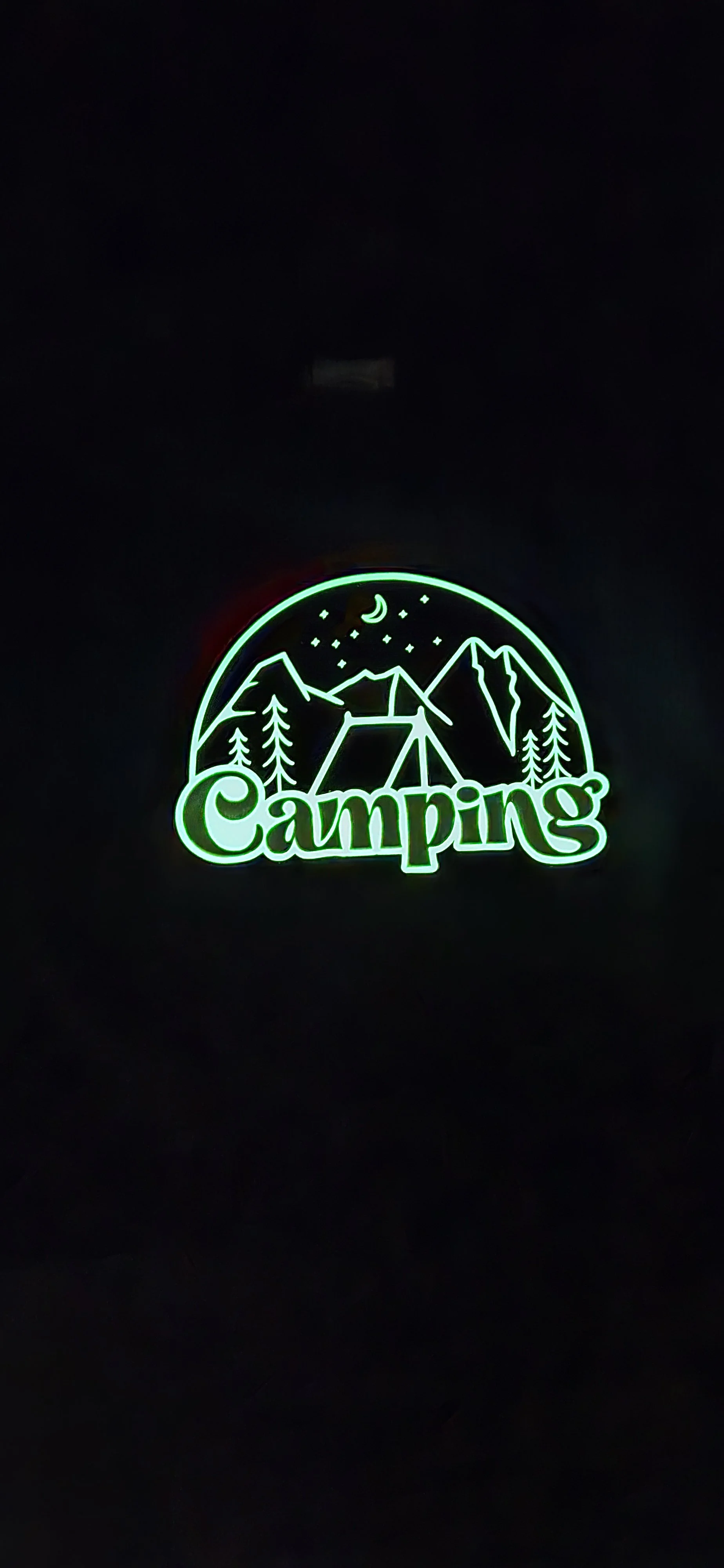 Glow-in-the-dark shirt design of a tent, mountains, and pine trees with the word Camping, glowing green in the dark