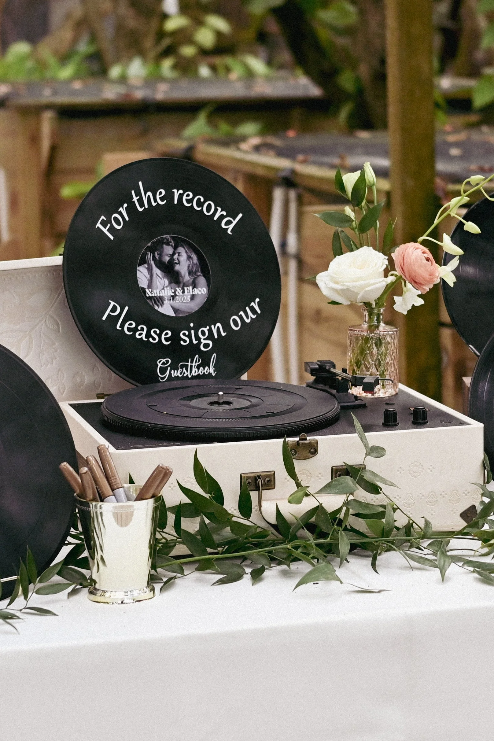 Vintage record player setup with vinyl guestbook idea at a wedding, decorated with greenery and flowers.