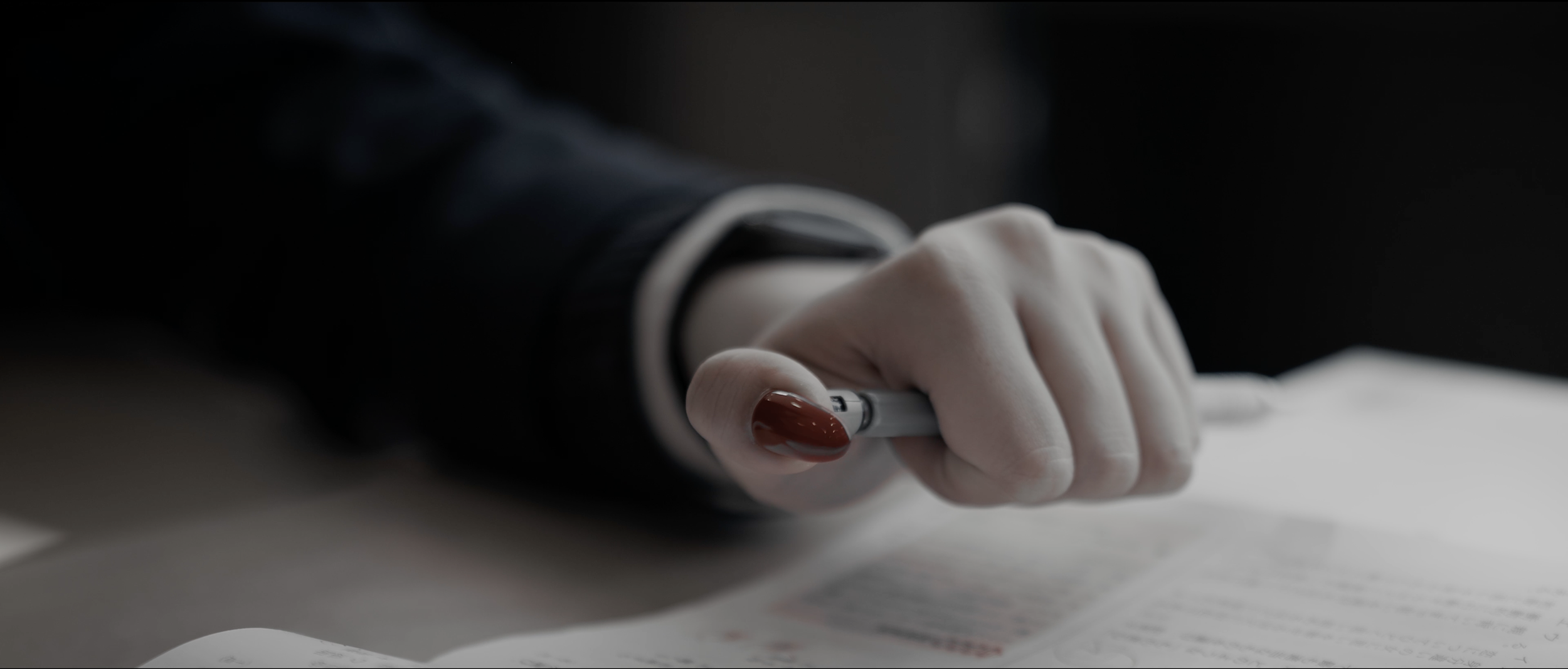 Close-up of a hand holding a pen and writing on a sheet of paper, with a dark background.