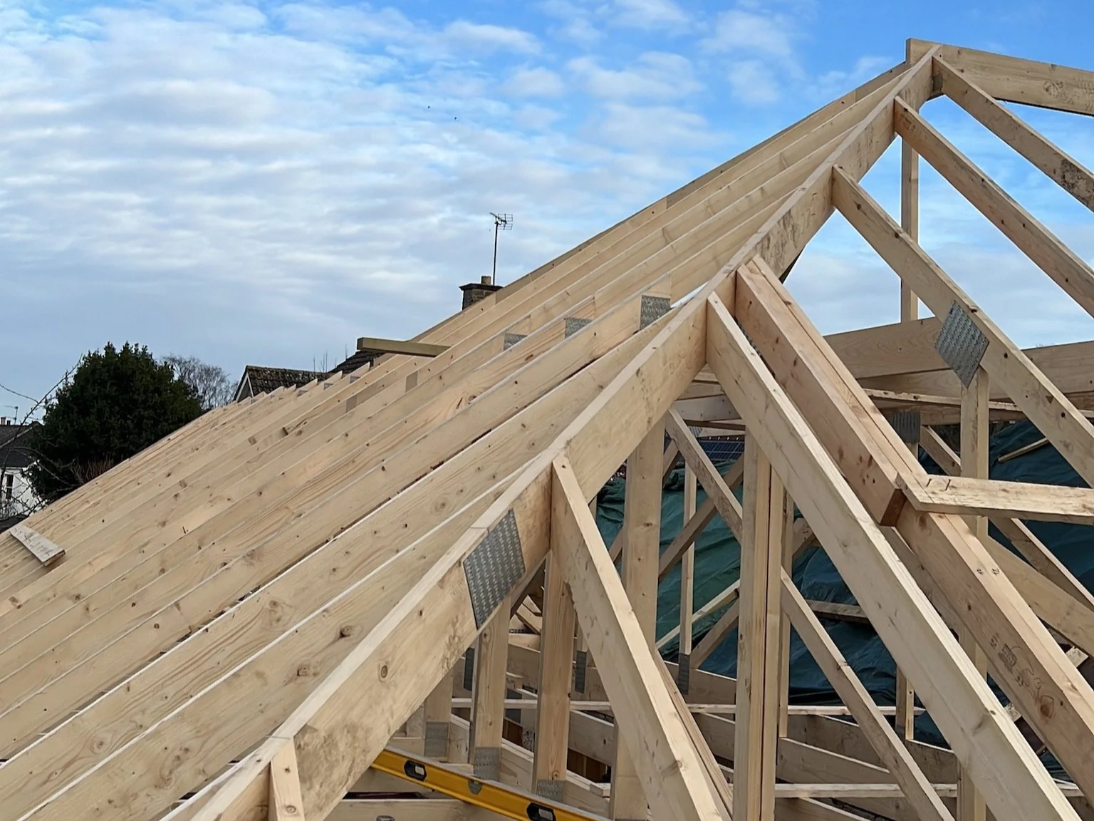 Wooden roof trusses under construction by Oaksmith Building Ltd on a residential building in The Cotswolds with blue sky and clouds in the background.