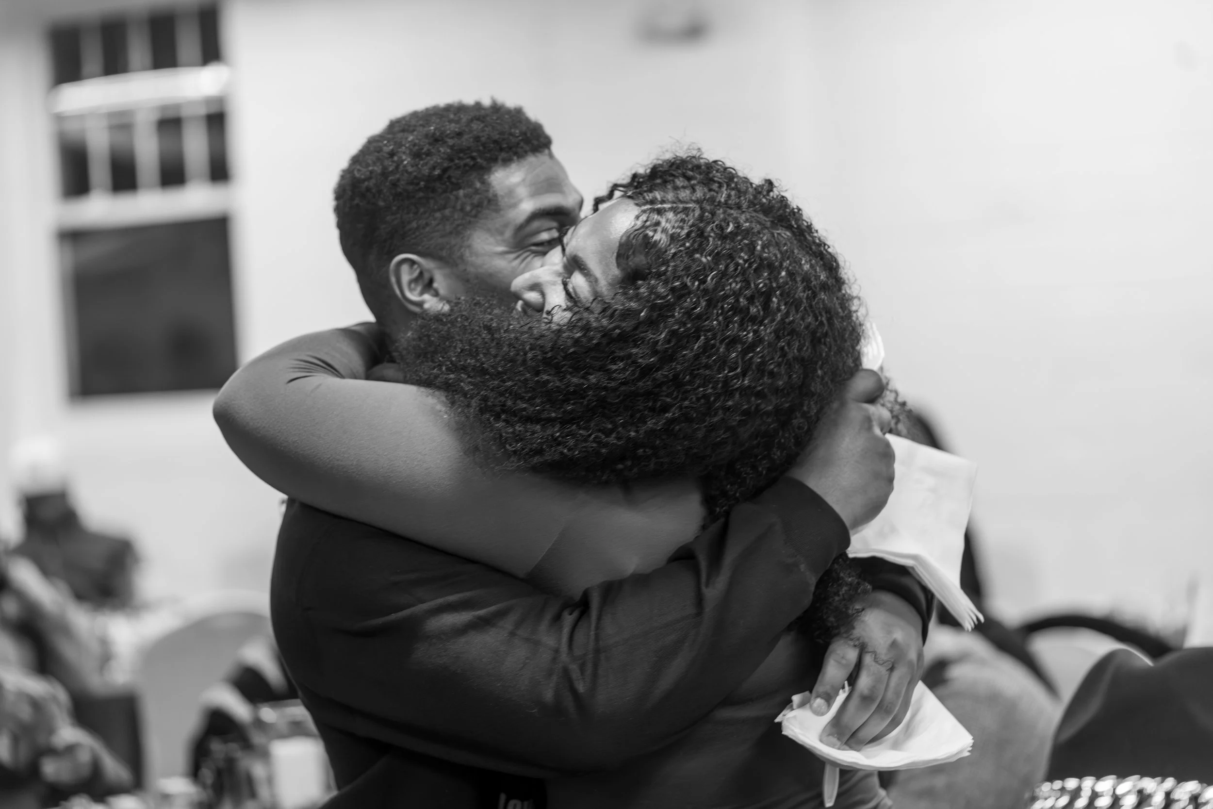 Two people hugging, smiling, and appearing happy in an indoor setting.