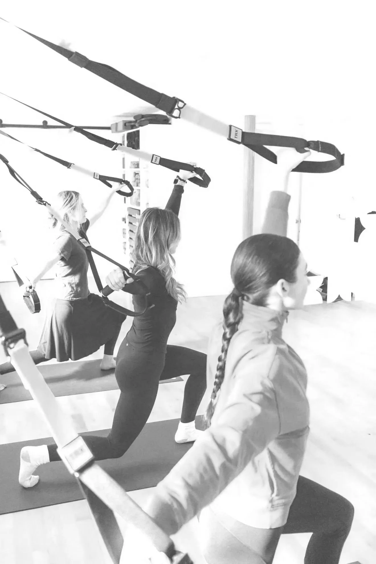 Women participating in a Pilates or strength class using TRX suspension trainers.