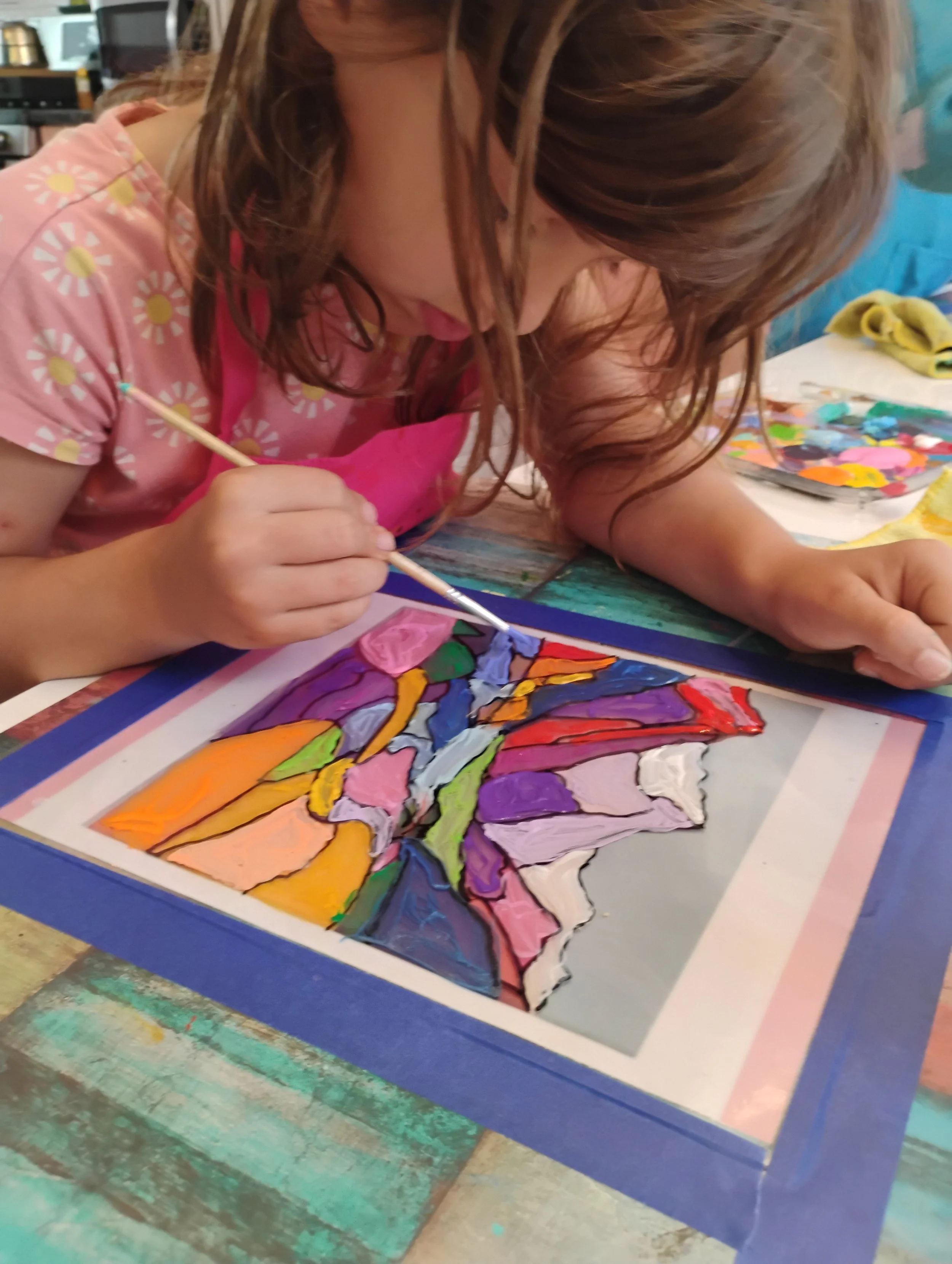 A young girl with brown hair painting a colorful picture on paper at Lunisa summer camp.