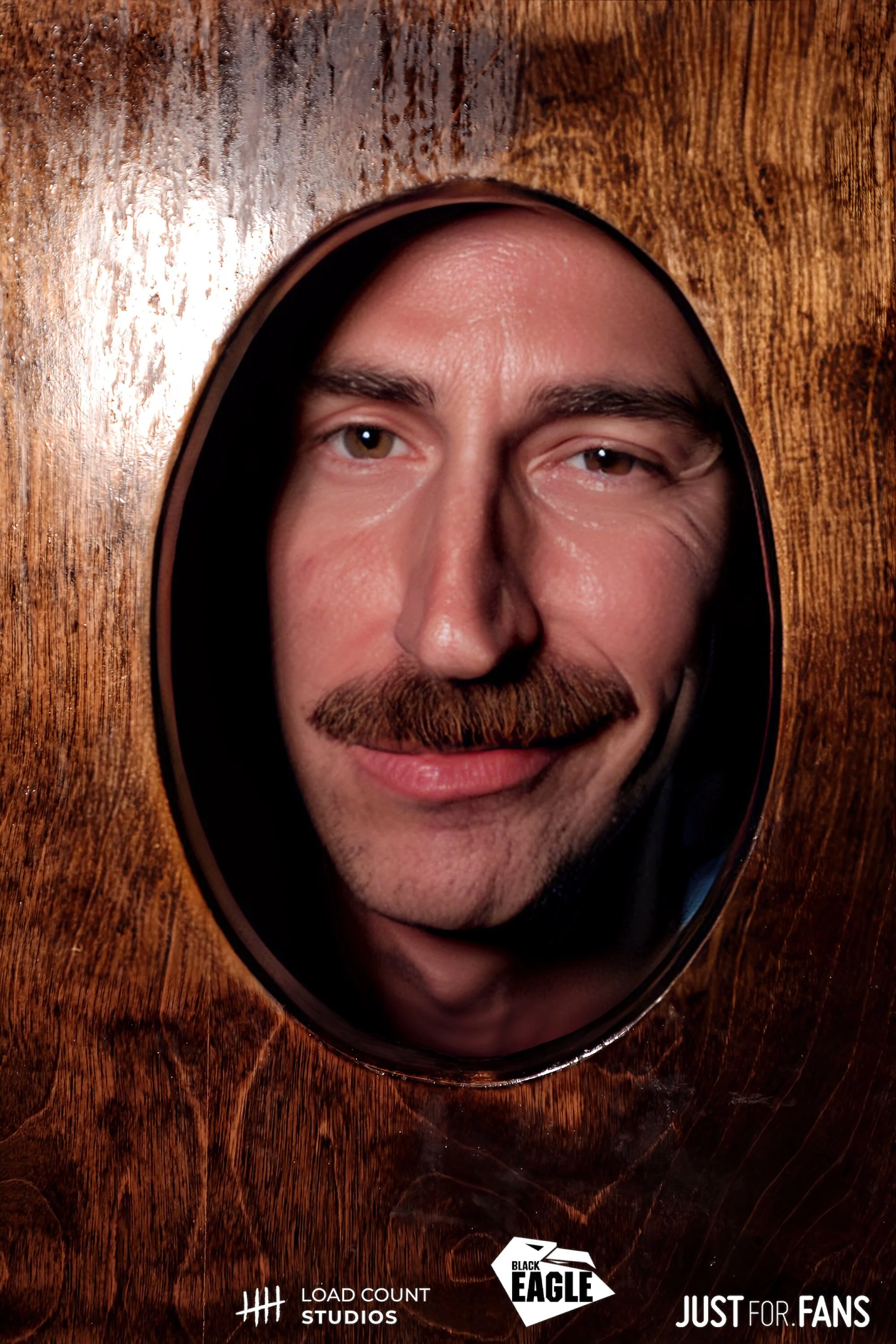 A man with a mustache peering through an oval opening in a wooden surface. Logos for Load Count Studios, Black Eagle, and Just For Fans are visible.