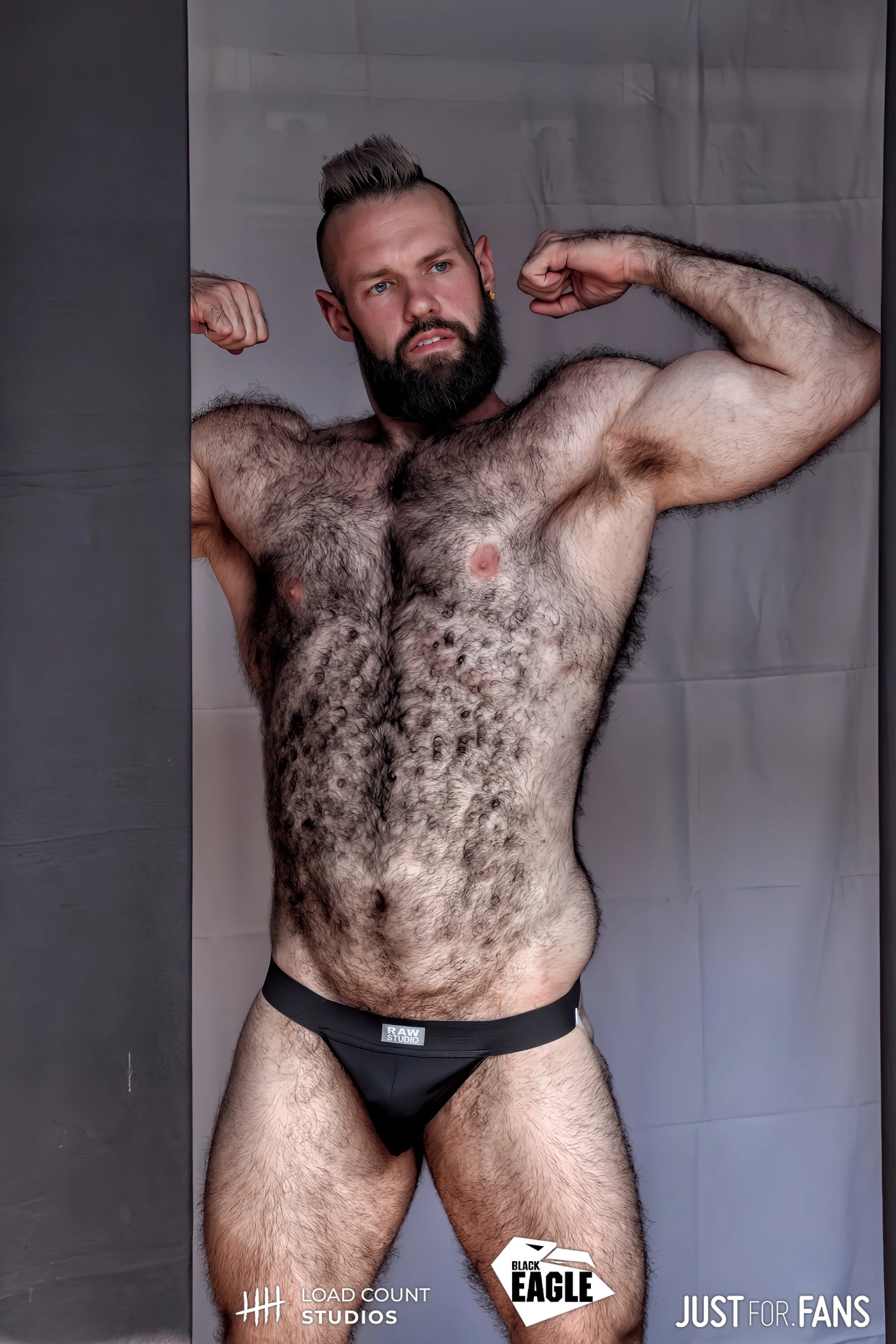 Bearded, muscular man posing in black underwear with arms flexed.