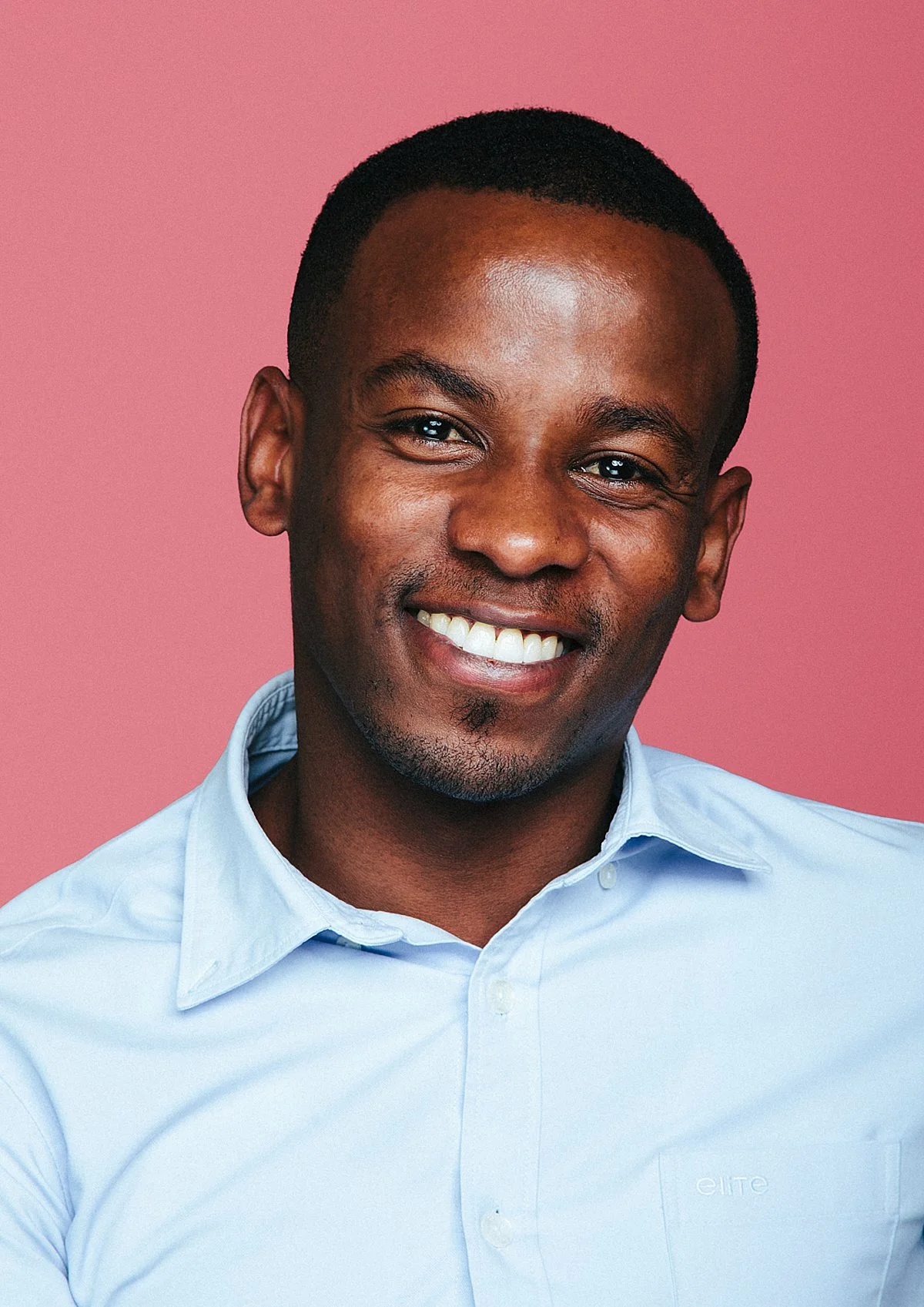 Studio headshot: smiling portrait on a pink background