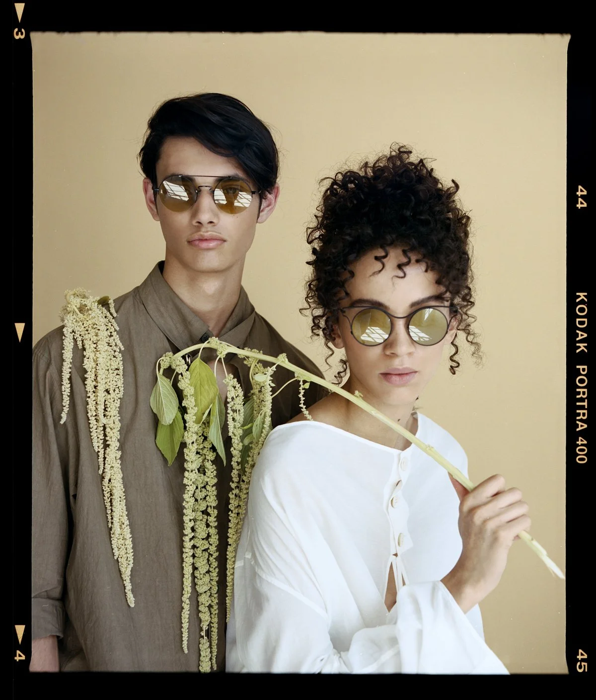 Eyewear campaign: two models in sunglasses holding a leafy branch