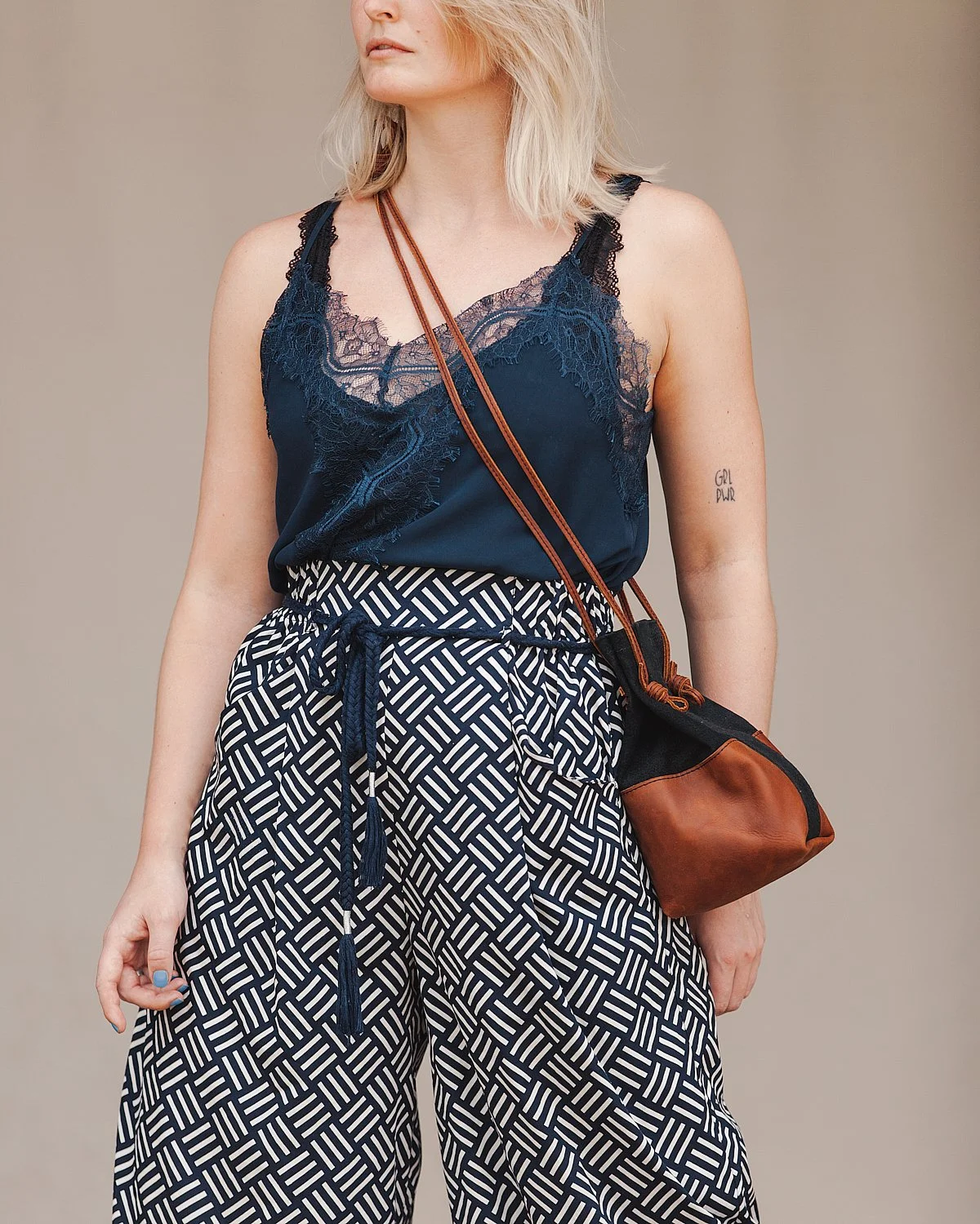 A woman with blonde hair wearing a navy blue lace top, patterned wide-leg pants, and carrying a brown and black shoulder bag.