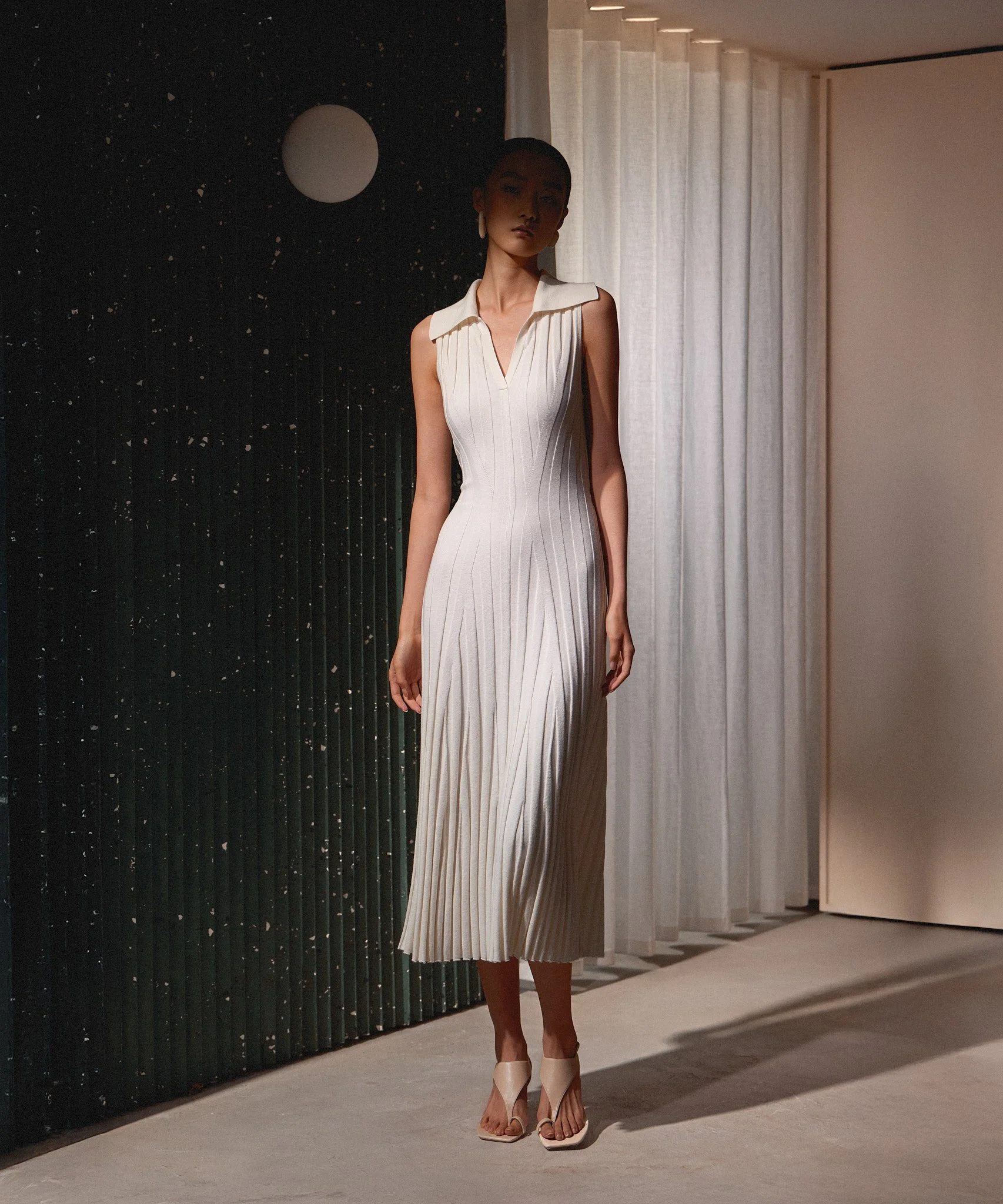 Fashion lookbook: model in a pleated white dress and heels, shot indoors