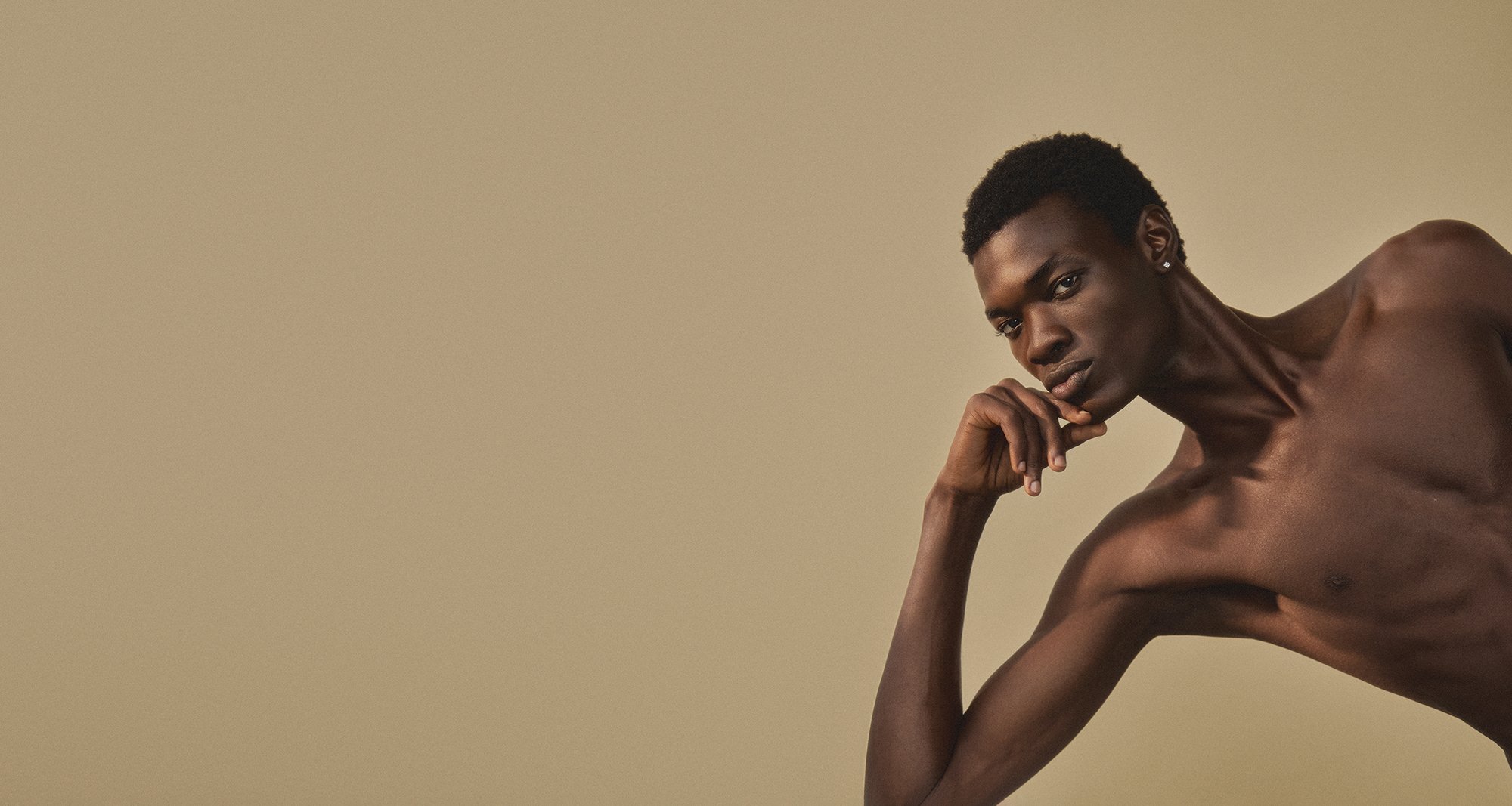 Model test: studio portrait of a model leaning on one elbow against a warm sand backdrop