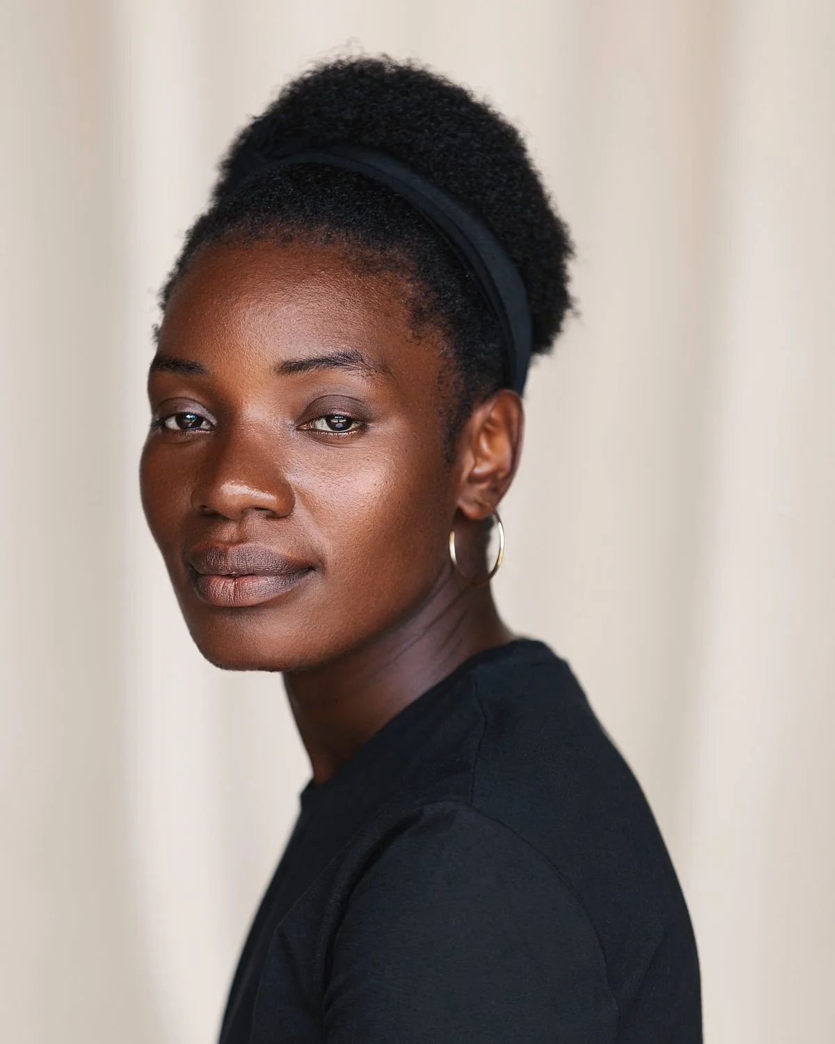 Portrait of a Black woman with short natural hair, wearing hoop earrings and a black top, looking at the camera with a neutral expression.