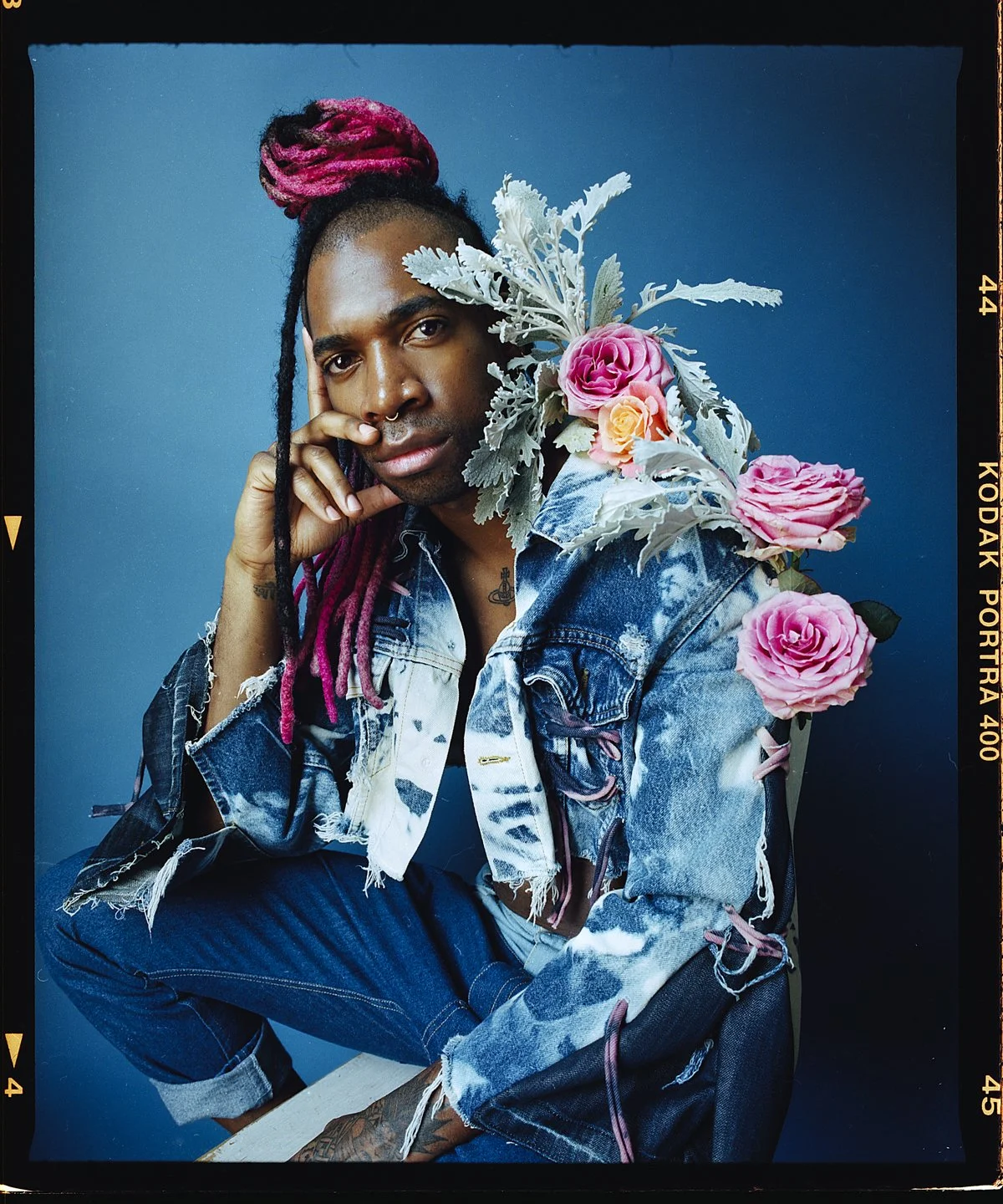 Studio portrait: pink locs and a distressed denim jacket on blue