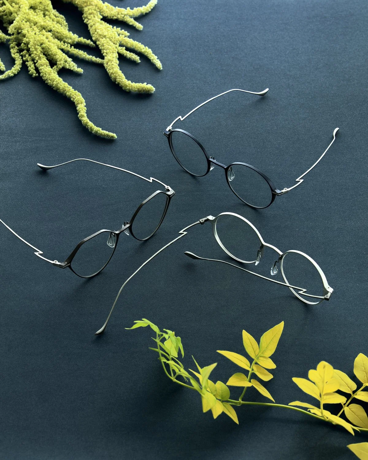 Eyewear still life: three thin metal frames on dark, dressed with foliage