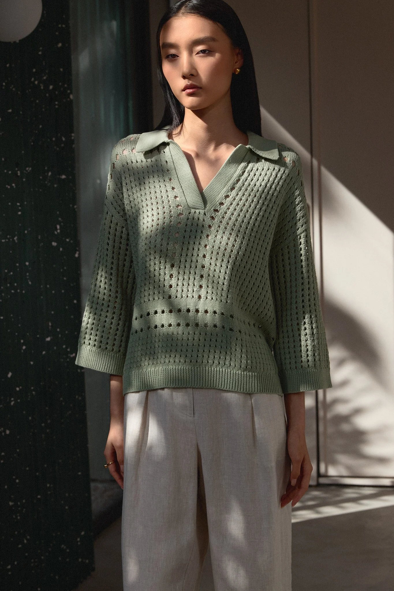 Fashion lookbook: model in a green perforated knit and cream trousers