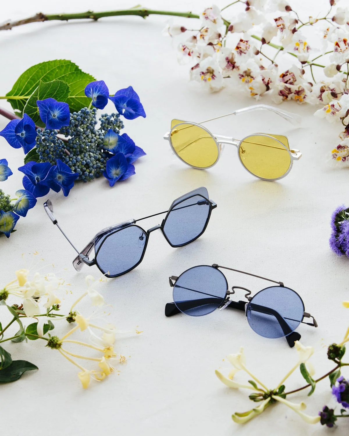 Eyewear still life: three coloured-lens sunglasses among cut flowers