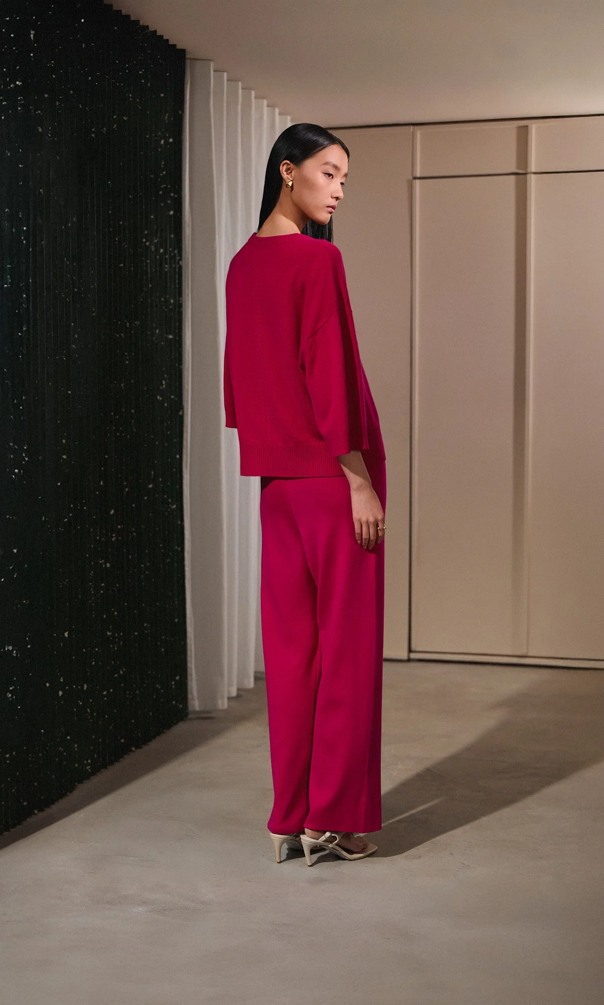 Fashion lookbook: model in red, shot side-on in a modern interior