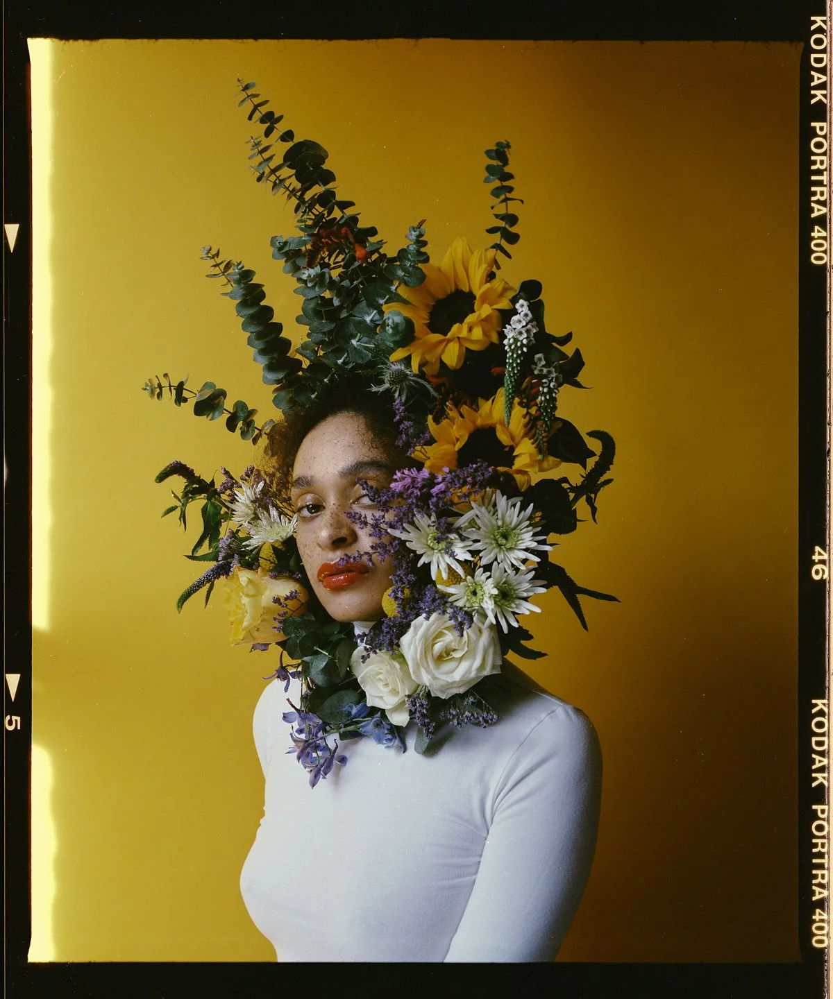 Studio beauty portrait: sunflower and rose headpiece against a yellow backdrop
