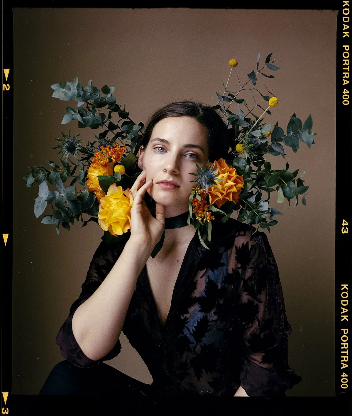 Floral studio portrait: model resting her chin on her hand among yellow and blue blooms